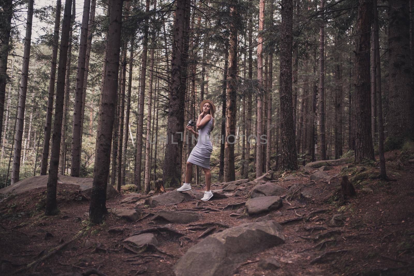 Slavic tanned fair-haired young girl with a boater hat on nature. Traveler tourist in a dark forest. constant tone of clothes. dark brown background