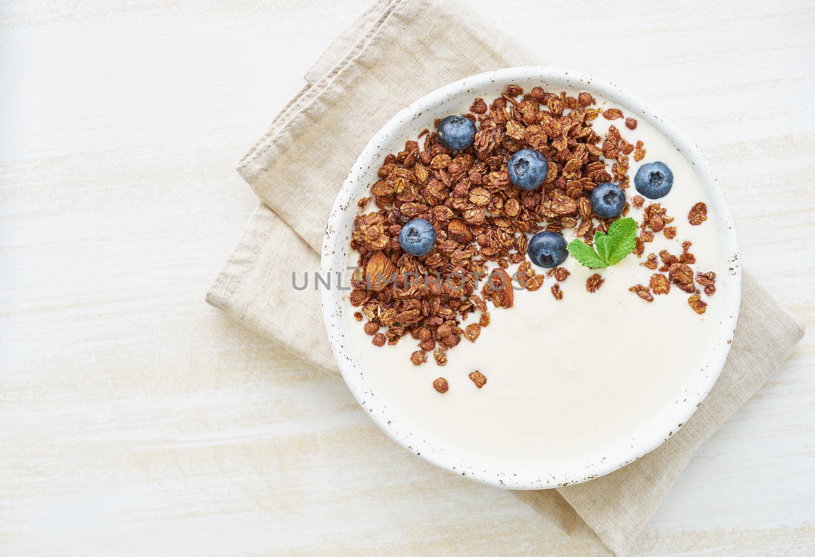 Yogurt with chocolate granola, bilberry. Breakfast on white rustic background, top view, copy space