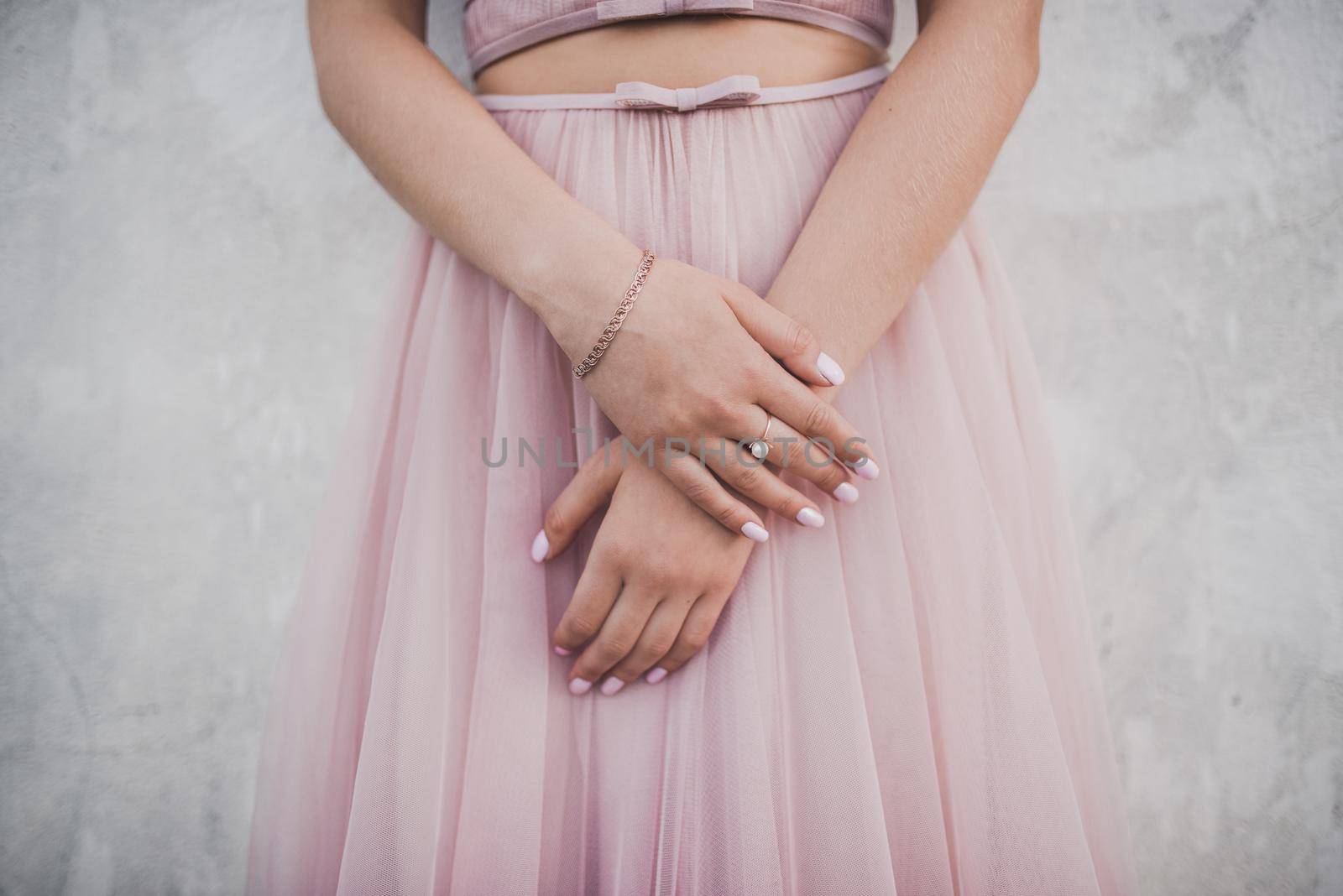 The female hands of the fair-skinned bride lie on the white wedding dress. A ring on the hand of a young girl.