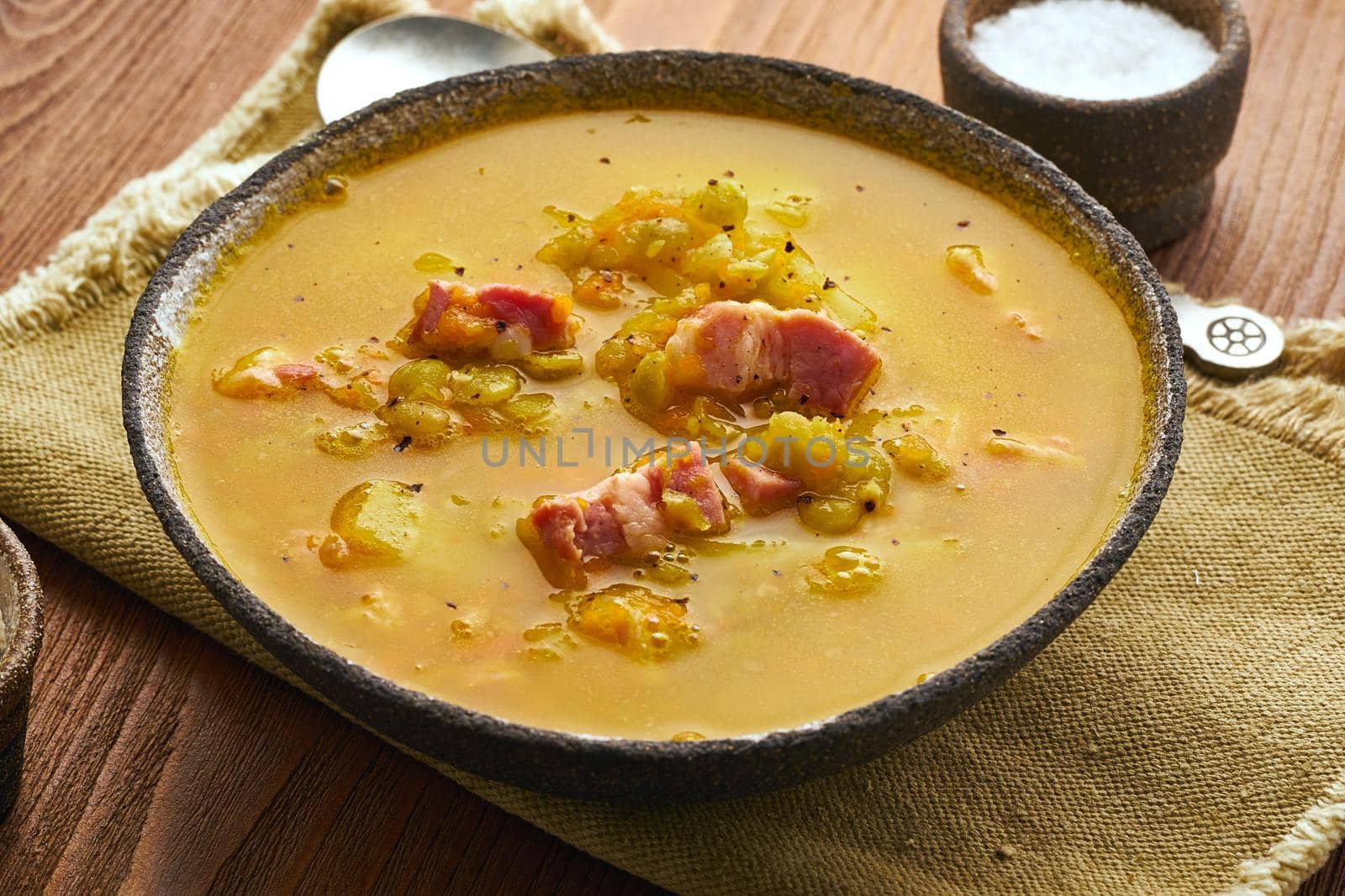 Winter hot soup with chopped green peas, pork, bacon, smoked on a dark brown wooden table. Delicious appetizing fat rich soup.