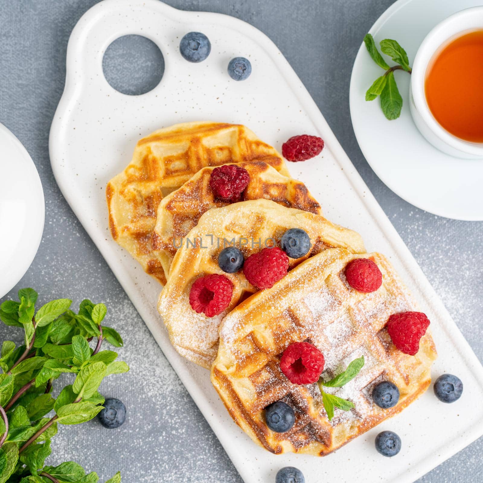 Belgian waffles with raspberries, blueberries, tea, top view. Healthy homemade breakfast, blue background