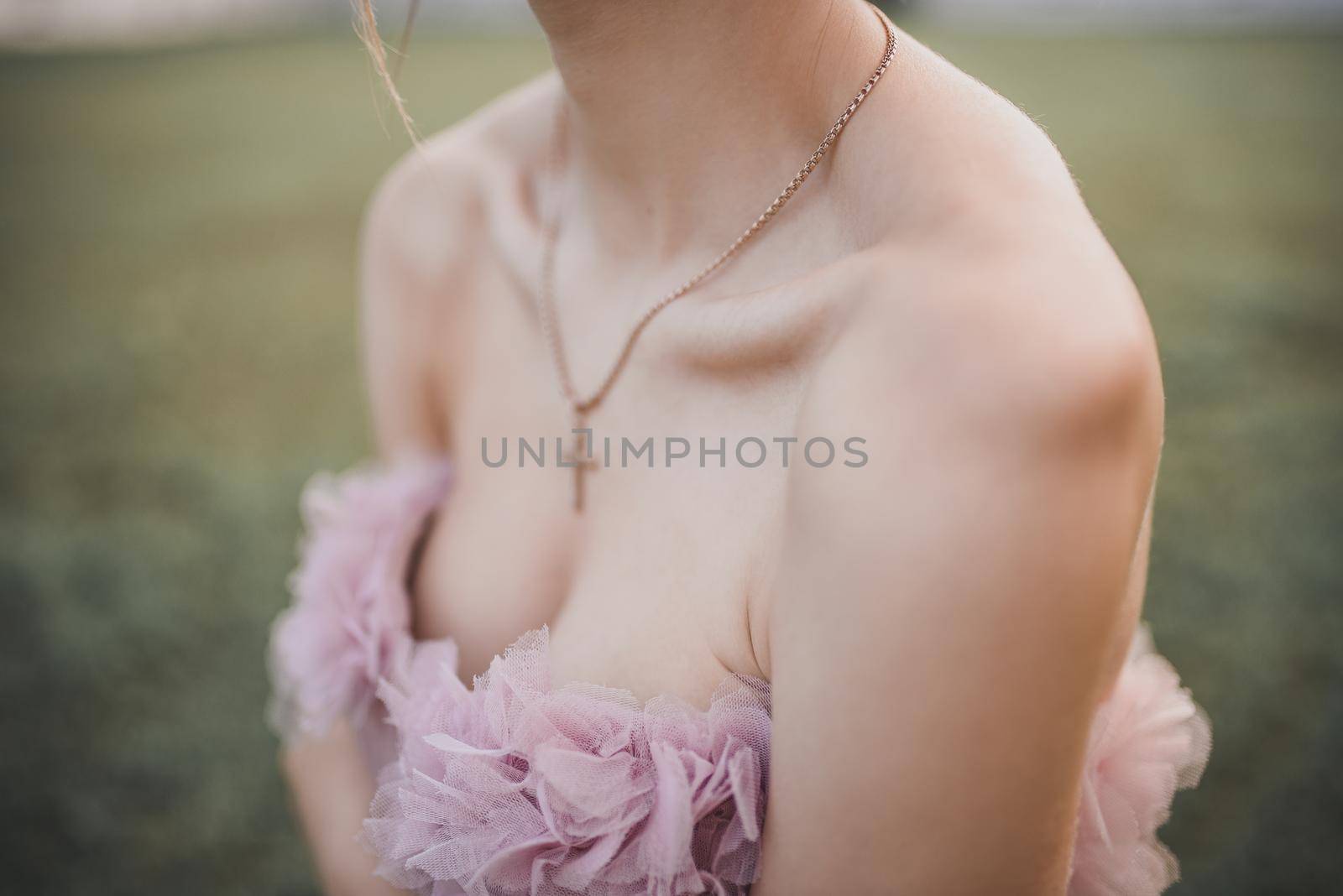 Young slim girl in elegant evening pink festive dress stands on the green background