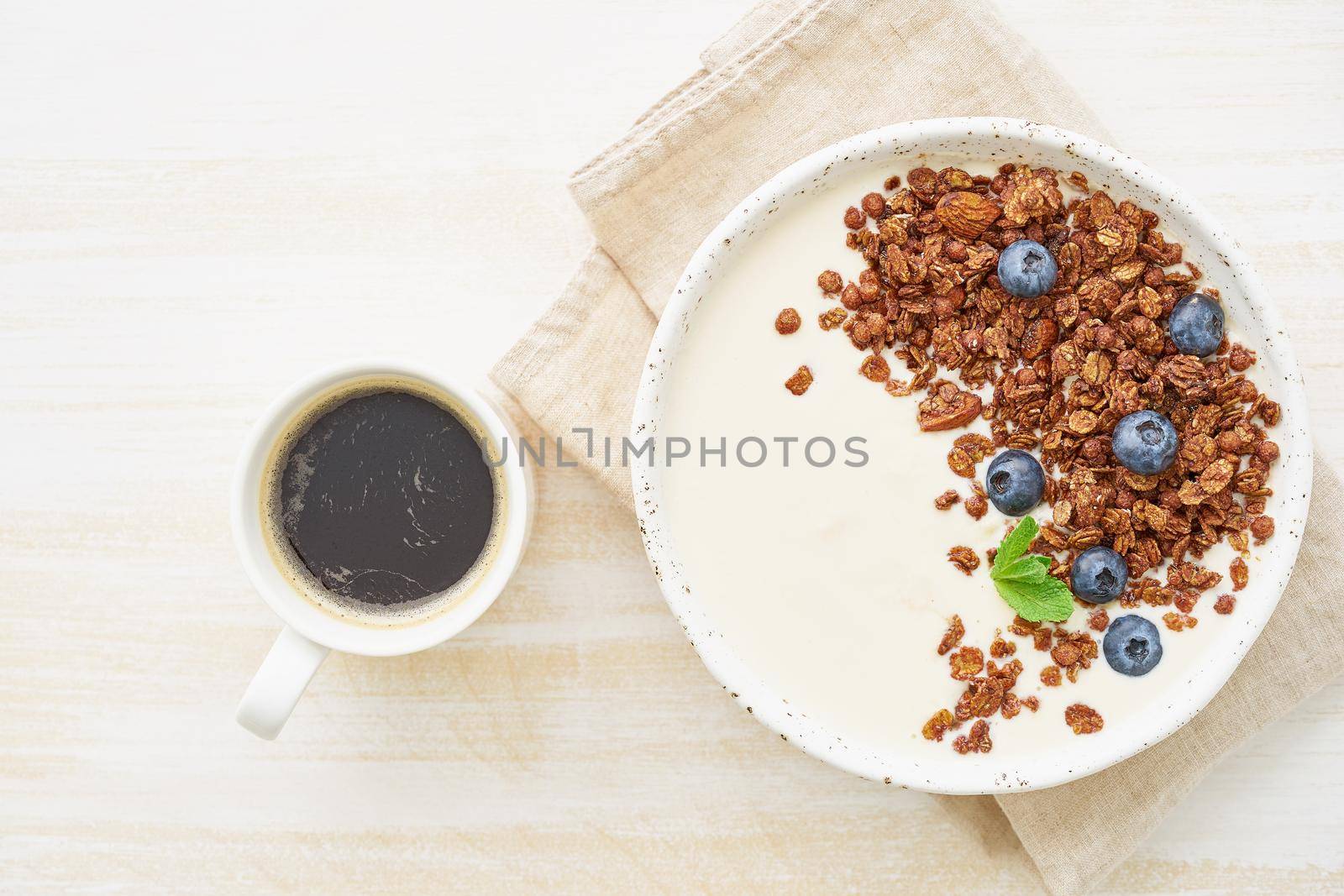 Yogurt with chocolate granola, bilberry. Breakfast with cupof coffee on white background, top view