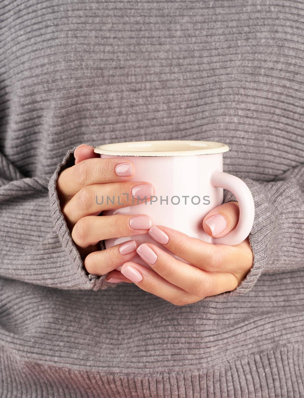 morning hot coffee at work in office on a cold autumn morning, hands holding a mug with a drink, gray sweater, pink manicure, close up, vertical
