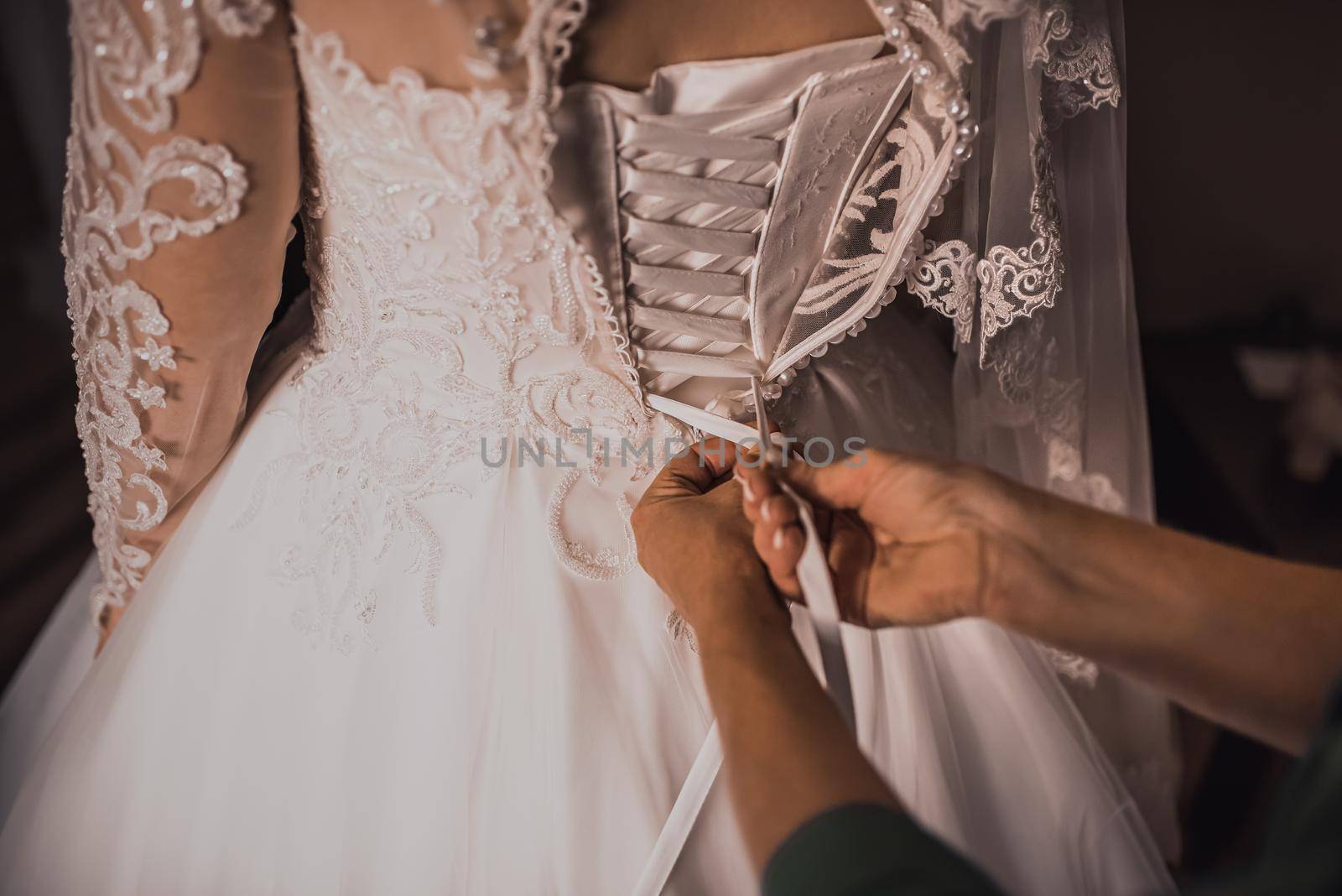 The back of the bride in a wedding dress. Mom's and woman's hands help fasten the clasps at the back.