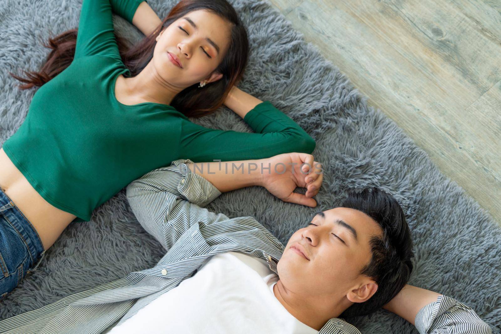 Happy Asian couple lying together on carpet at living room floor. Love relationship and lifestyle concept.