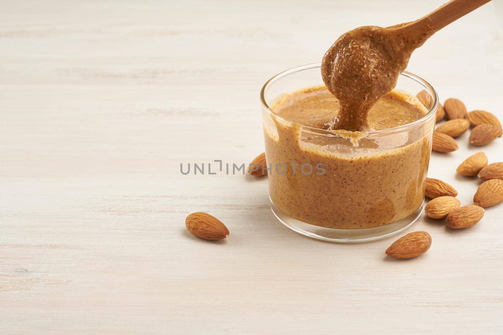 almond butter, raw food paste made from grinding almonds into a nut butter, crunchy and stir, white wooden table, copy space