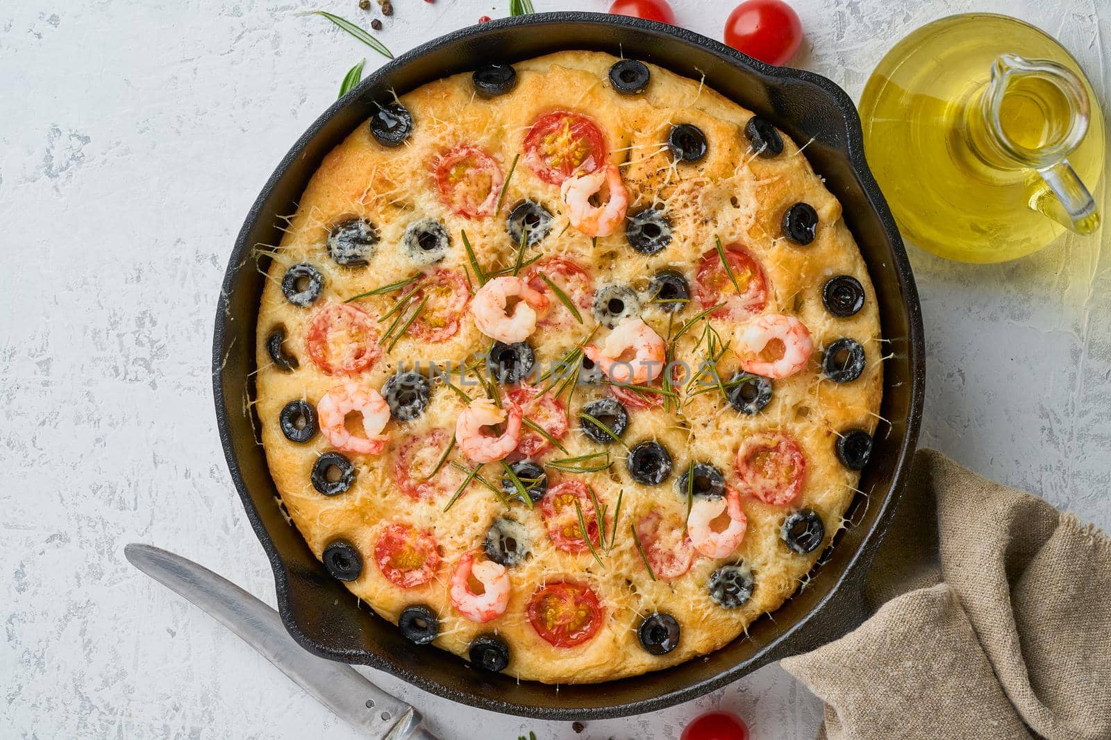Focaccia, shrimp pizza in skillet, italian flat bread with tomatoes, olives and a rosemary. Top view, copy space, white concrete background
