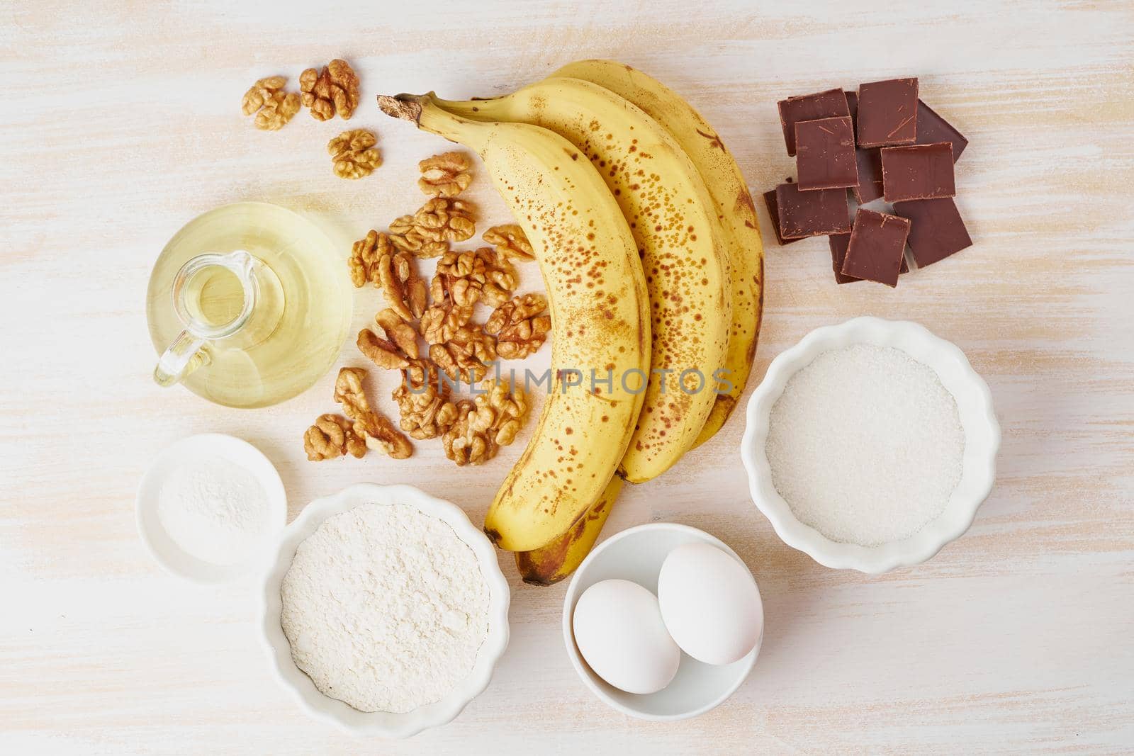 Ingredients for Banana bread. Step by step recipe. Banana, nut, chocolate, flour, egg, oil, sugar. White wooden table, top view