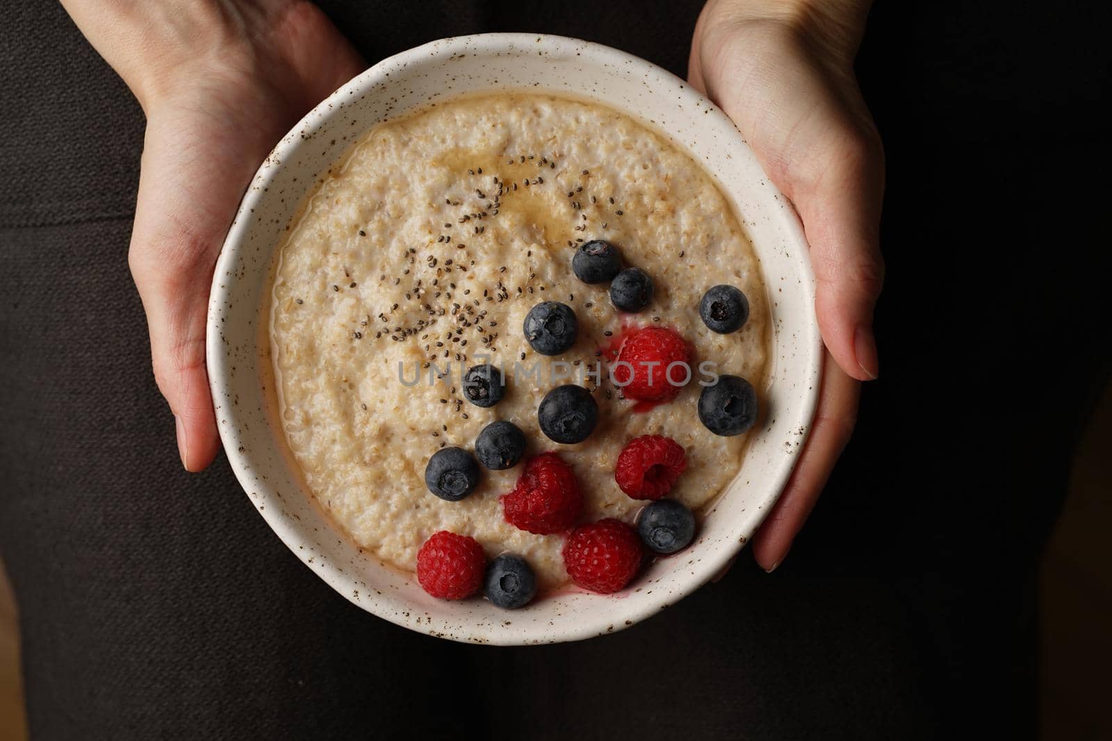 Plate with porridge in hand on dark background, top view. Healthy Breakfast with raspberries by NataBene