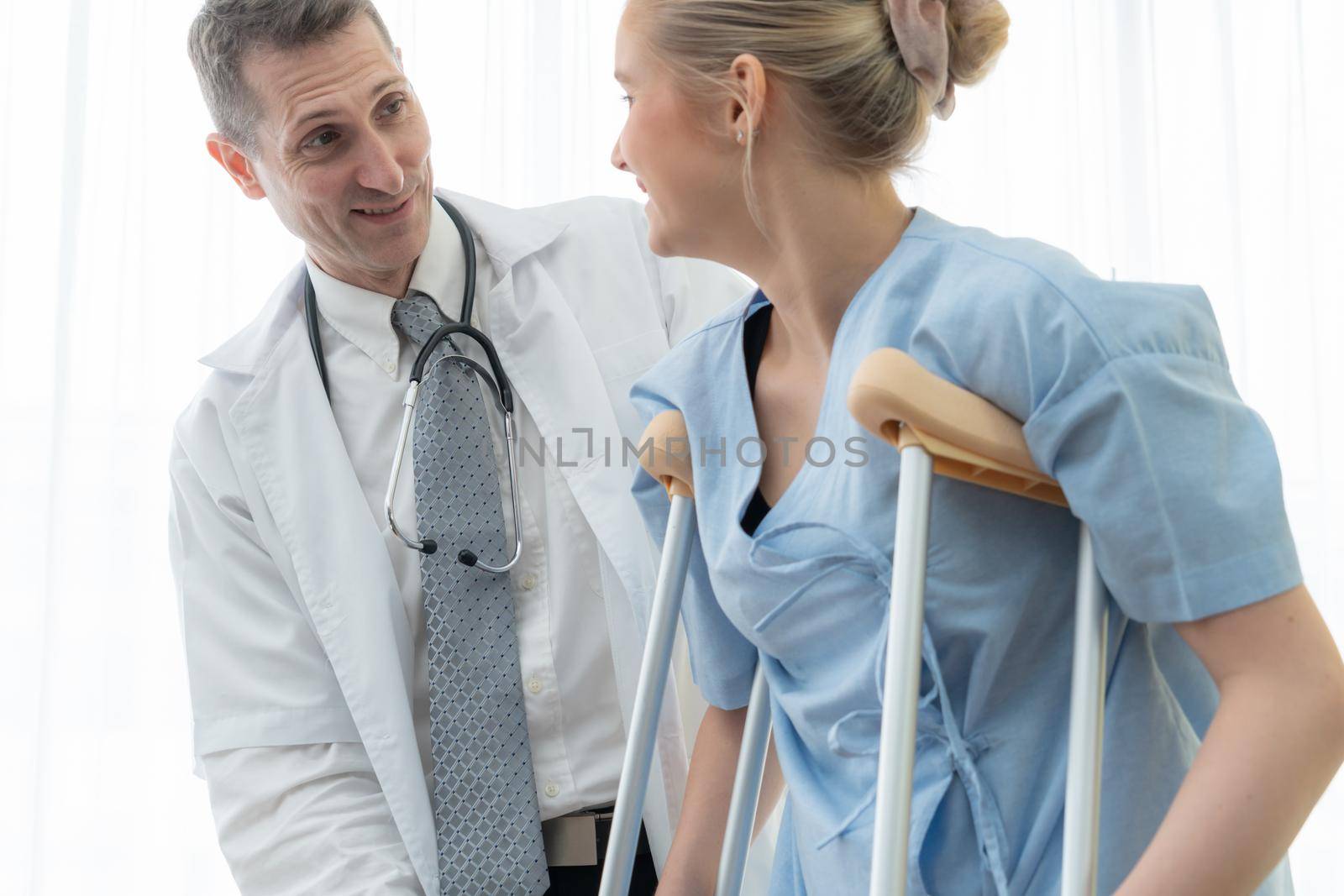 Doctor takes care of patient in crutch at hospital. Physical therapist and leg injury recovery concept.