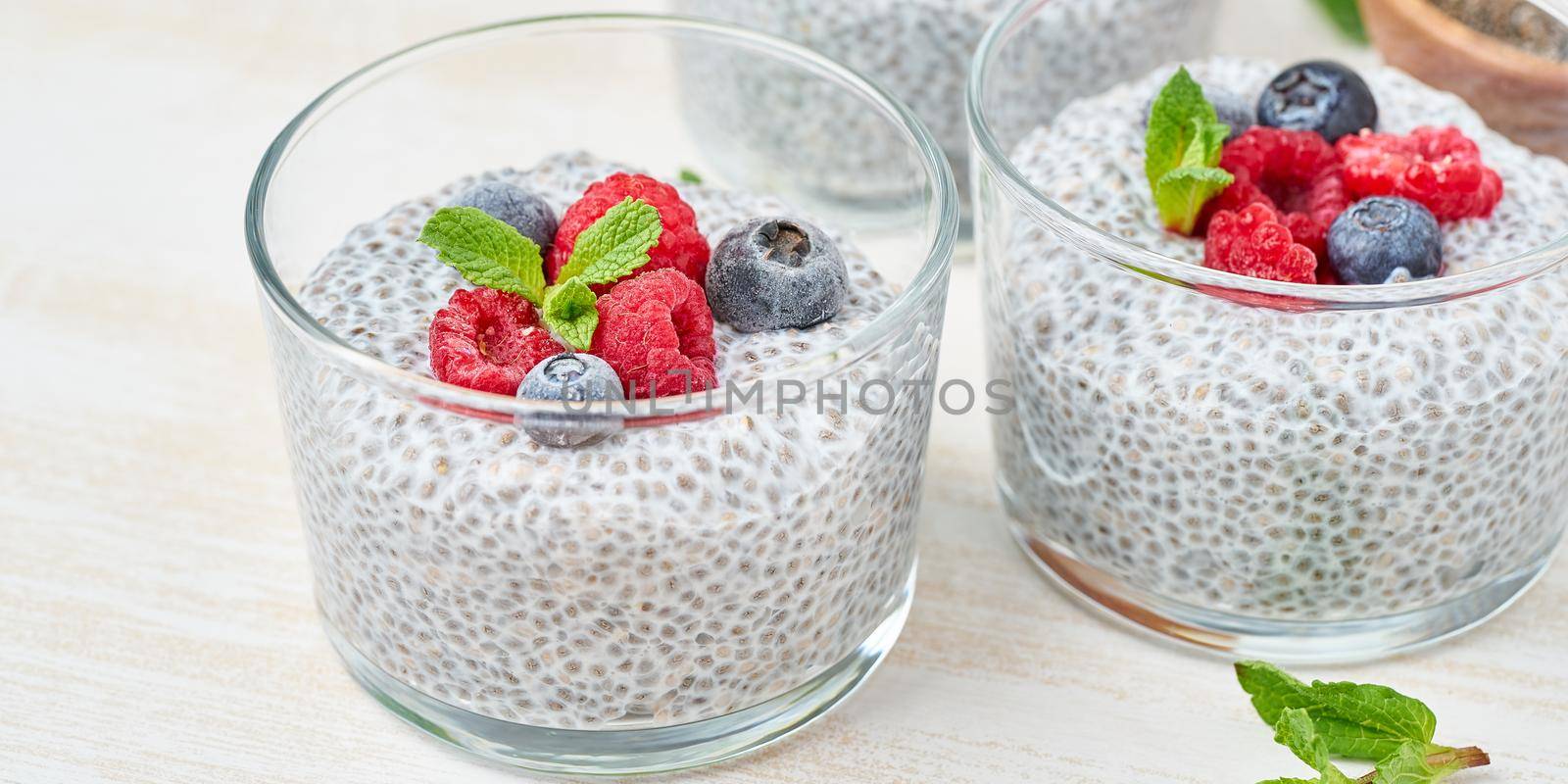 Banner with chia pudding with fresh berries raspberries, blueberries. Three glass, light wooden background, side view, flowers, close up