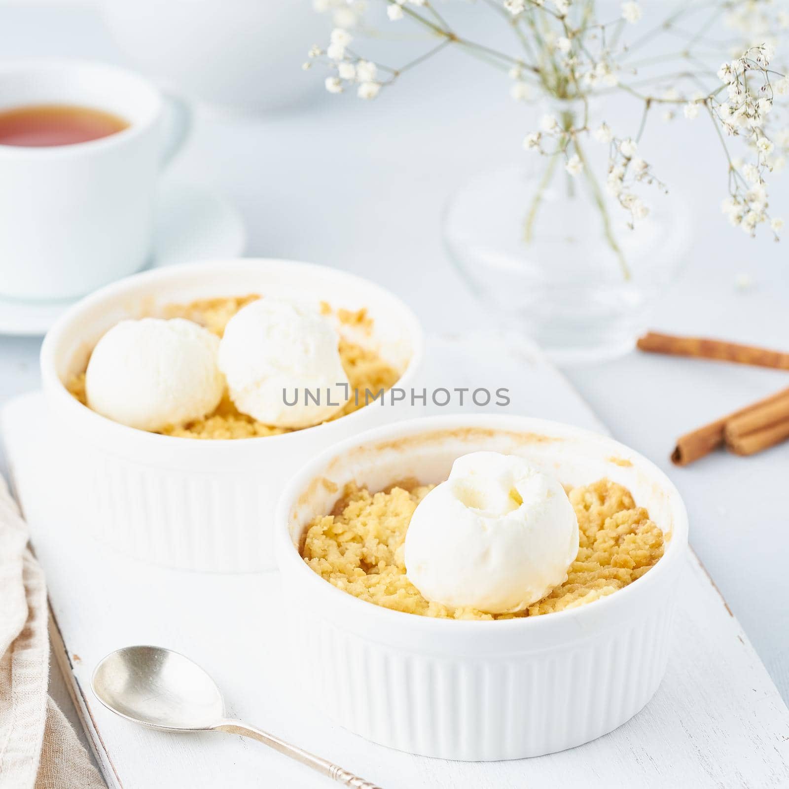 Close up apple crumble with ice cream, spoon with streusel. Side view, vertical. Morning breakfast on light gray table.