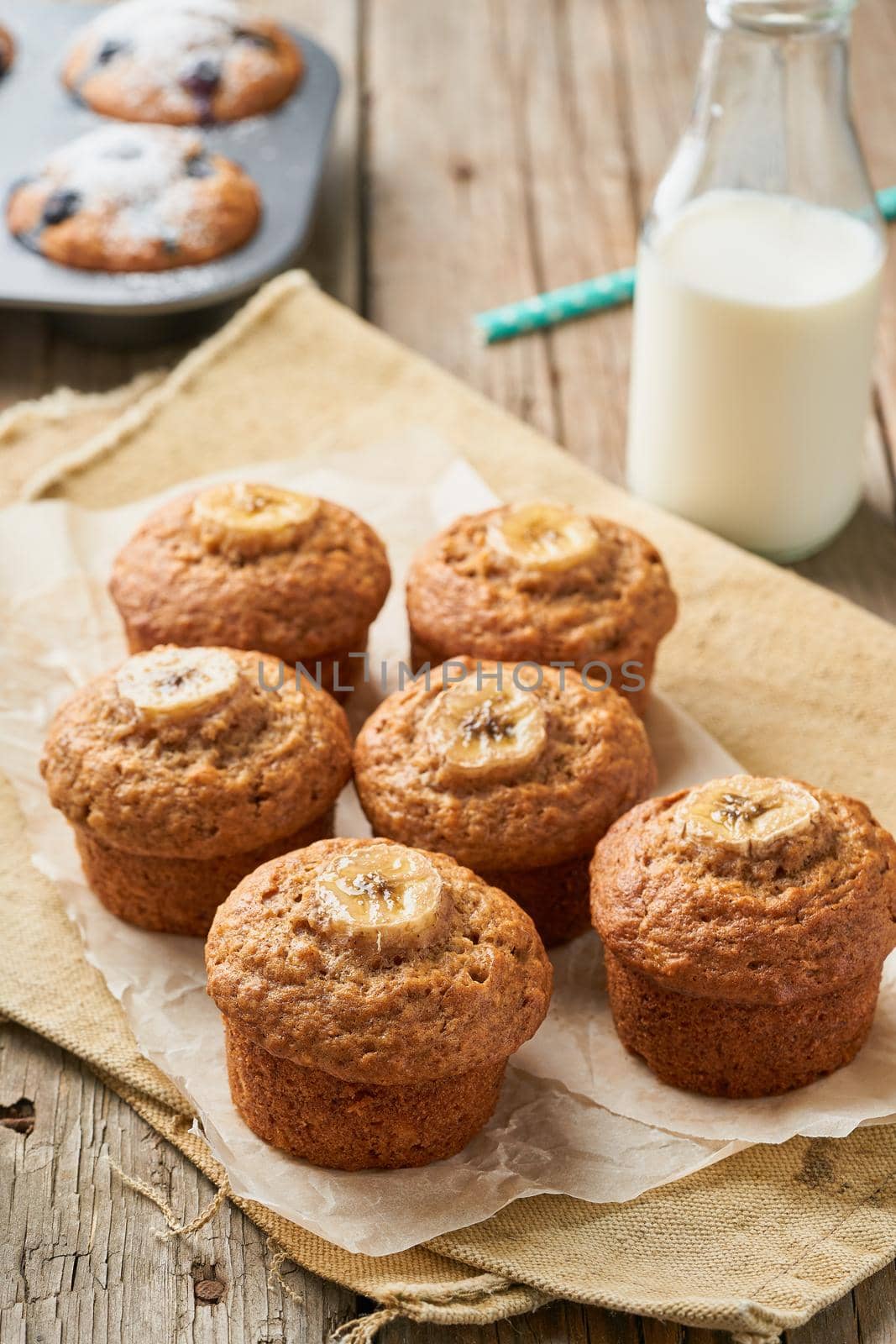 Banana muffin, side view, vertical. Cupcakes on old linen napkin, rustic wooden table, a breakfast with cake and milk