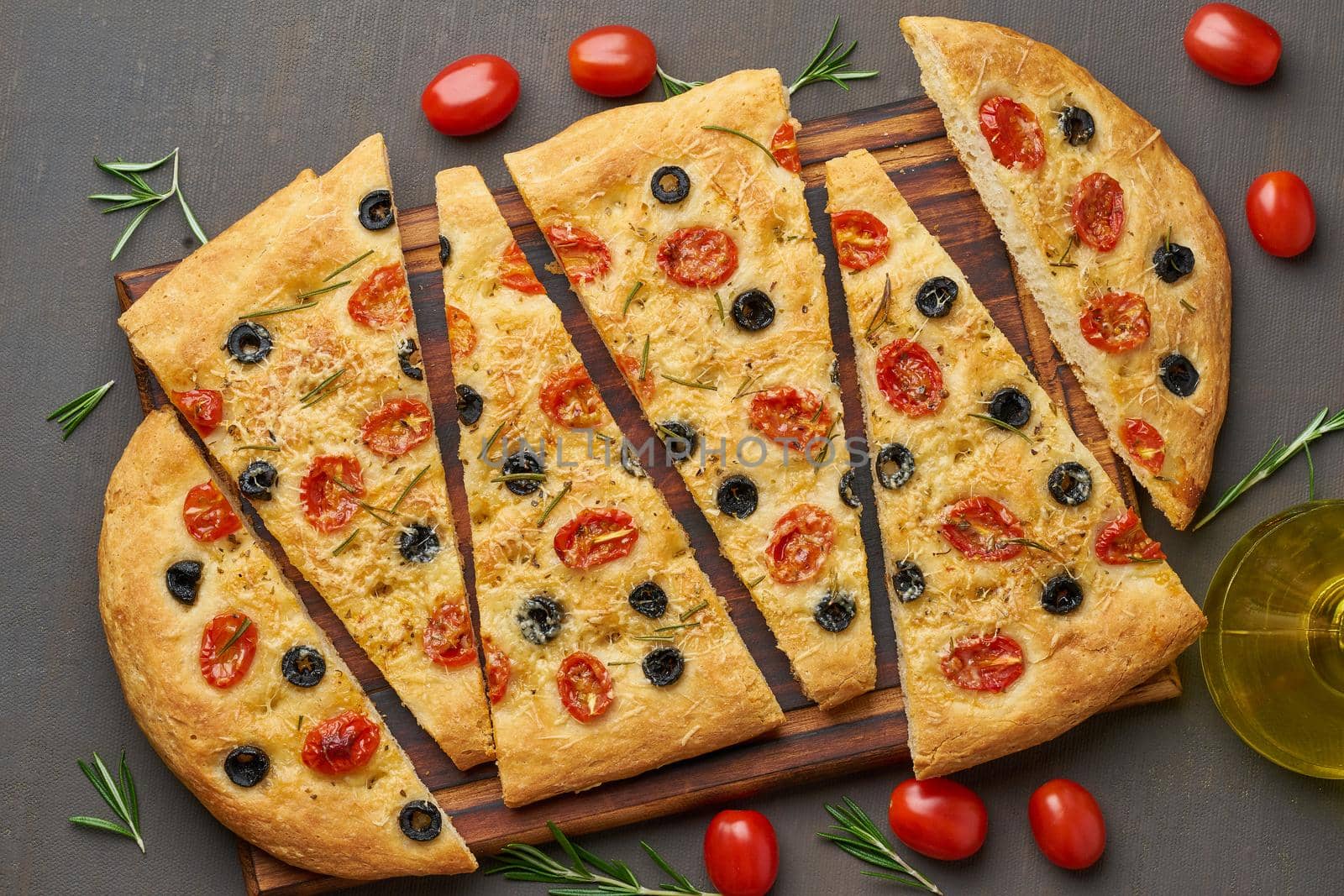 Focaccia, pizza, italian flat bread with tomatoes, olives and a rosemary on dark brown table, top view