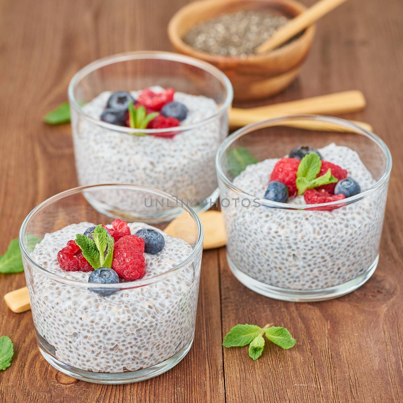 Chia pudding with fresh berries raspberries, blueberries. Side view, three glass on brown wooden background, close up