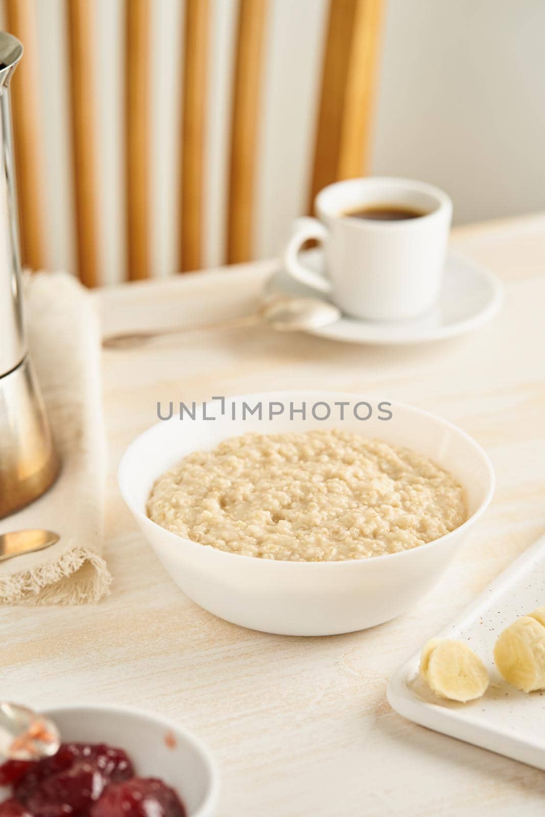 Oatmeal, large bowl of tasty healthy porridge for breakfast, morning meal. Vertical, side view, white wooden rustic table. Vegan diet