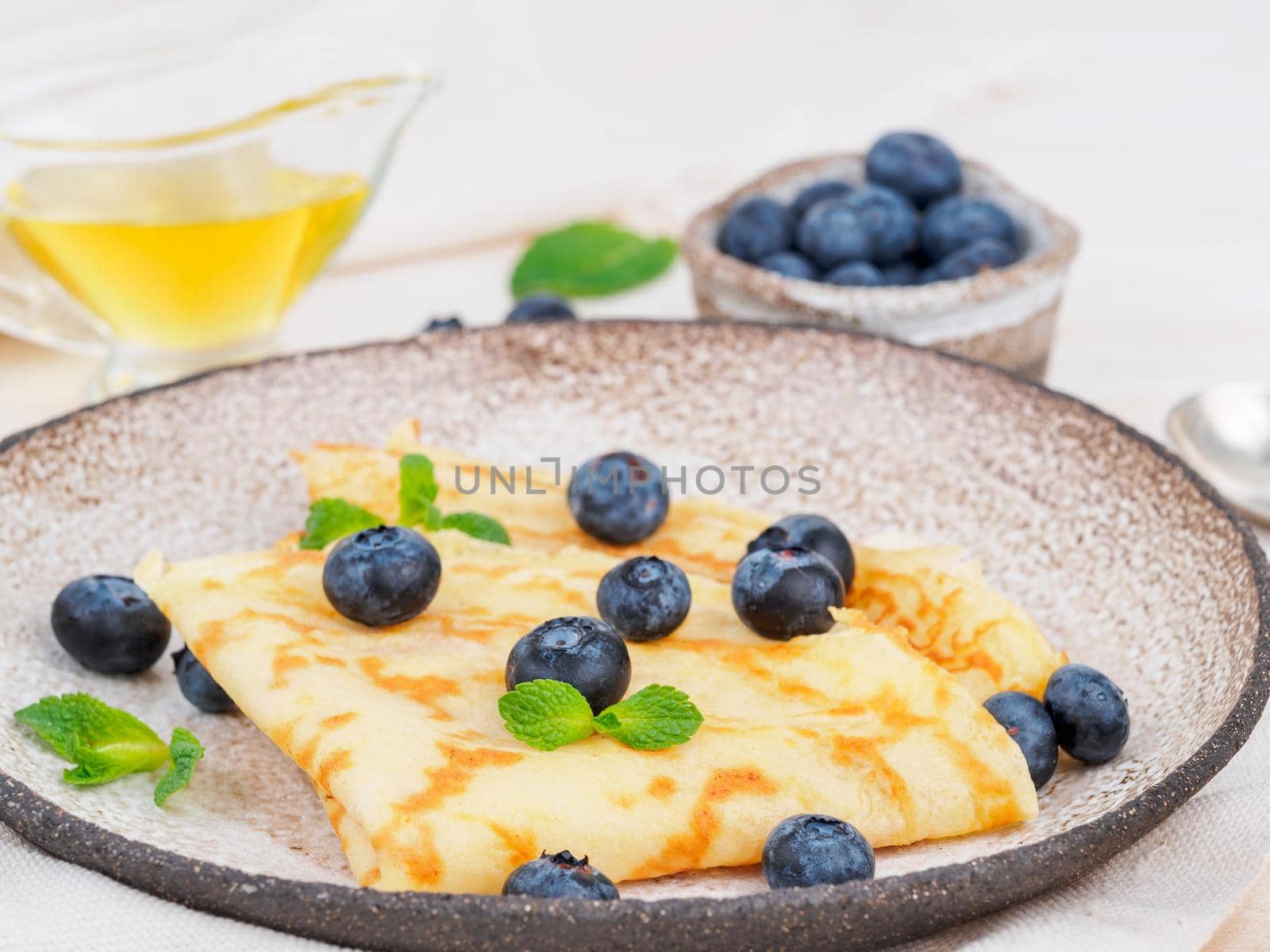Two pancakes with blueberries and mint on plate, side view, macro, close-up