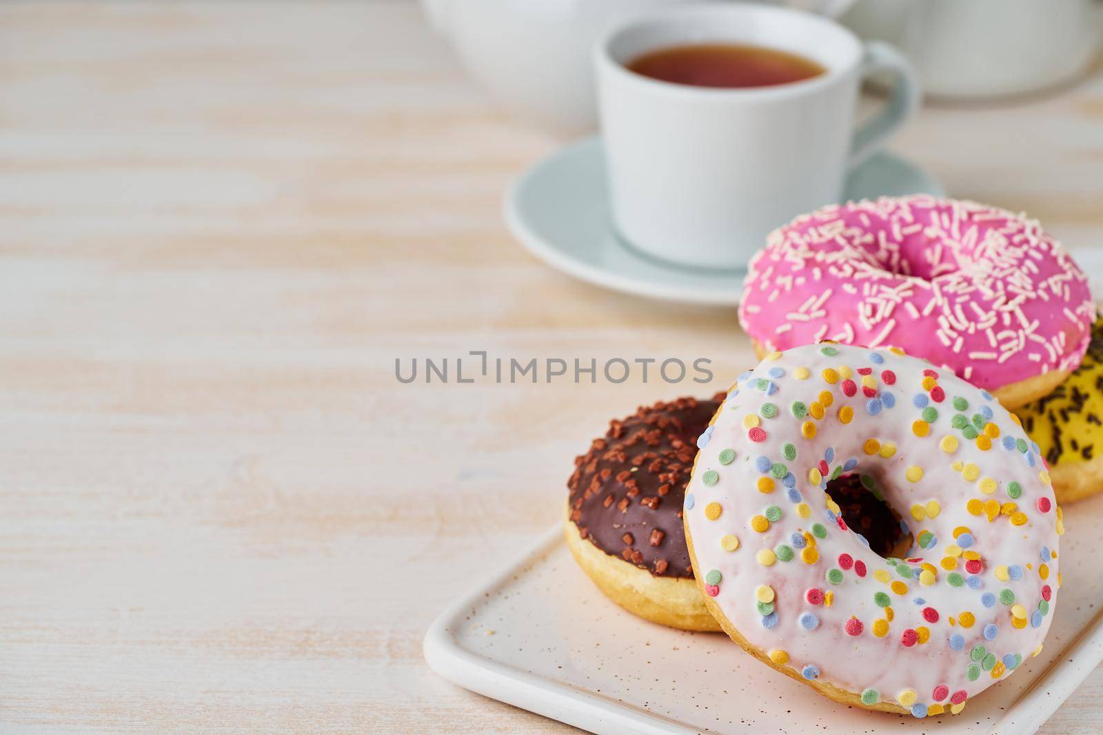 Doughnuts and tea. Bright, colorful junk food. Light beige wooden background. Side view, close up.