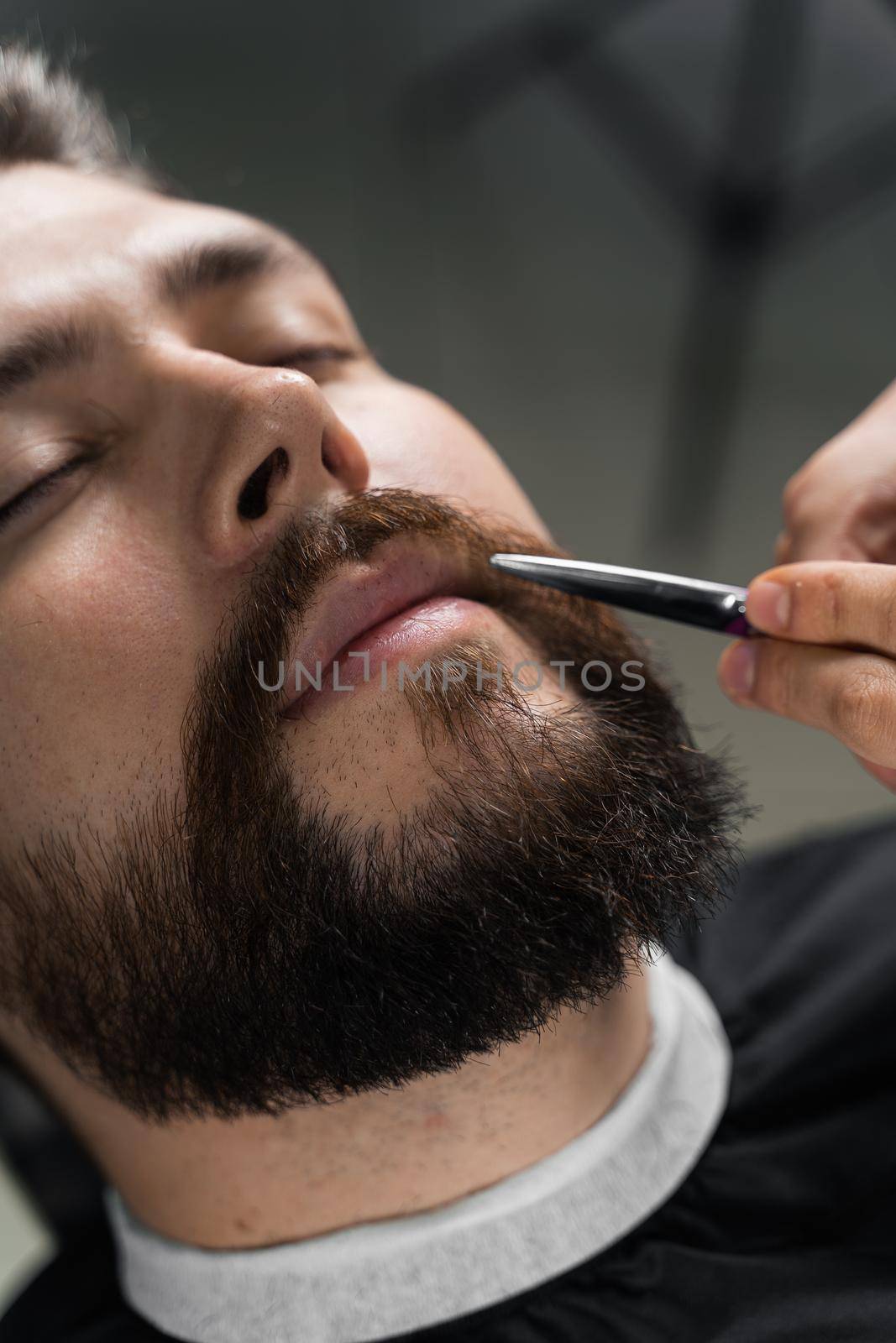 Haircut beard with scissors for a gentleman in a trendy barbershop. Professional hairdresser.