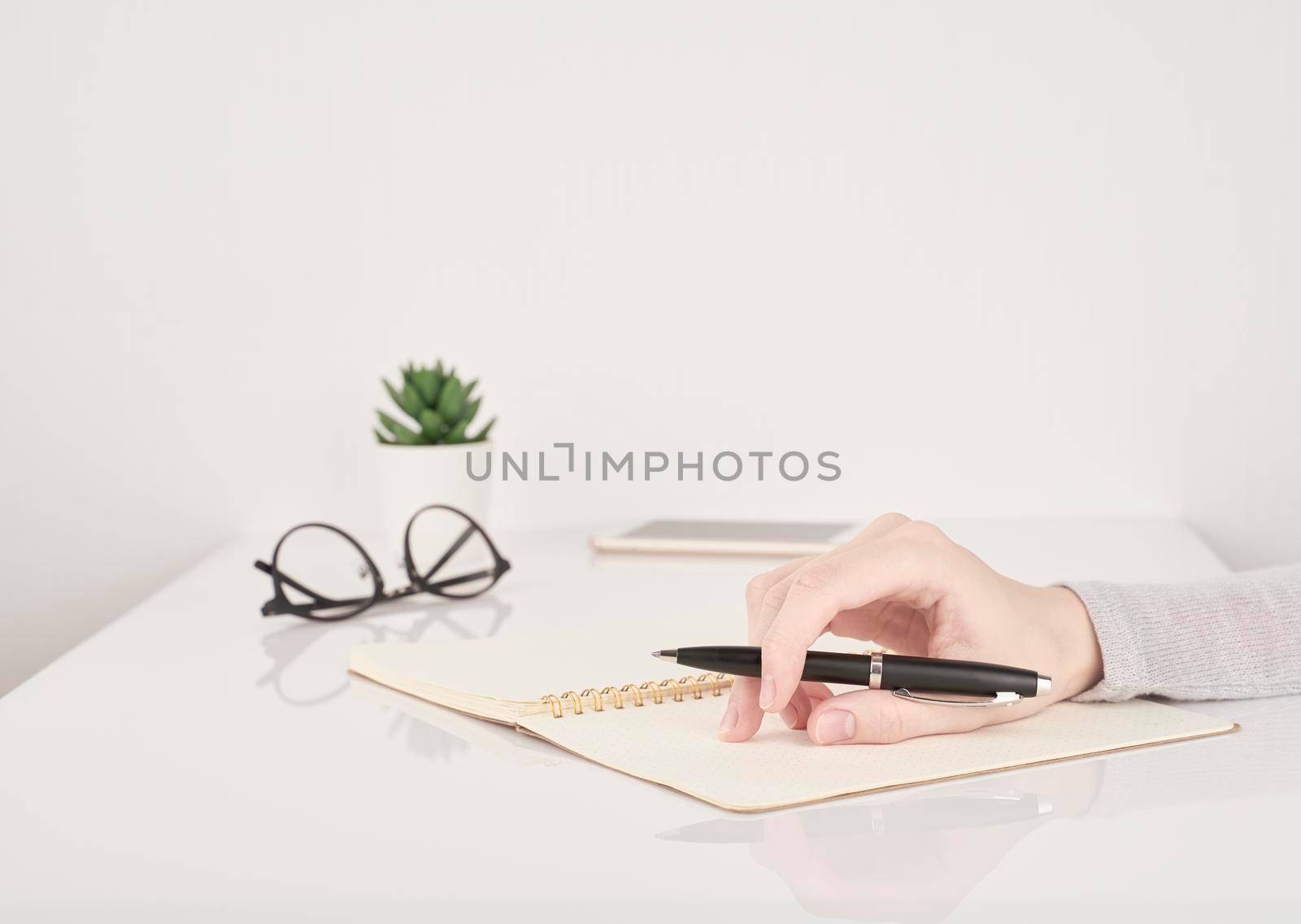 female young hand holding pen and writing on notebook page on white and gray background side view copy space