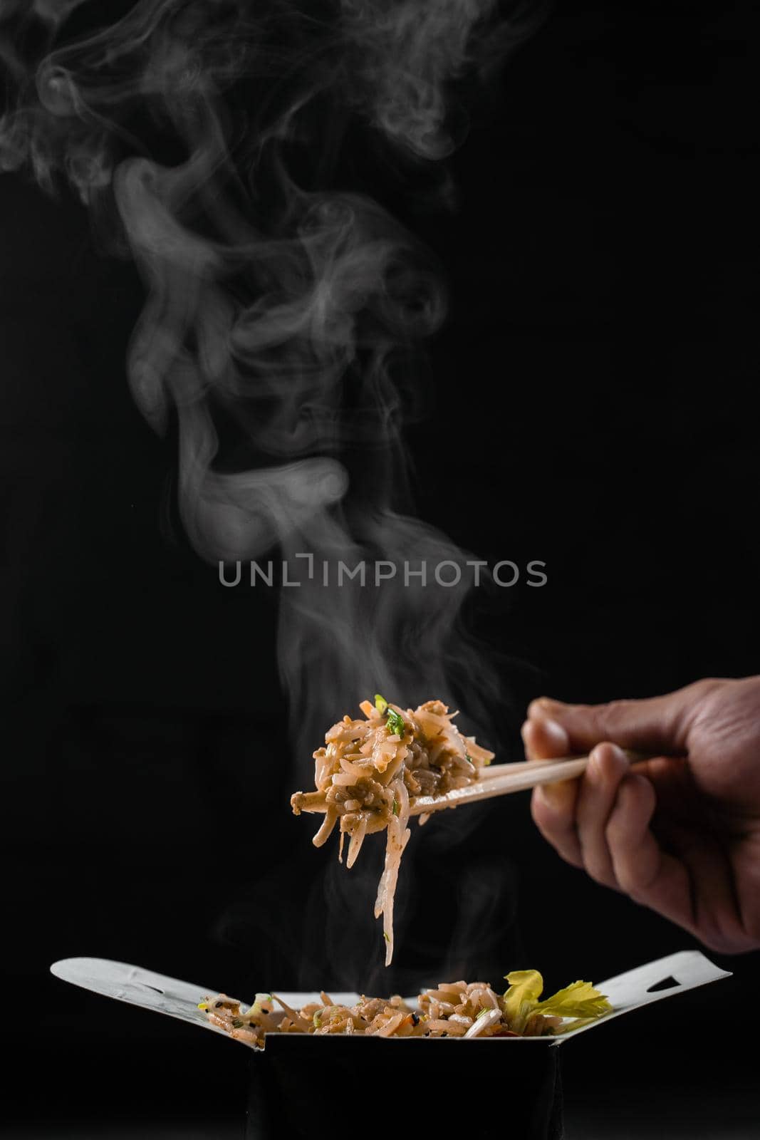 Steaming hot rice in wok box on black background. Holding rice with chinese chopsticks. Asian spicy dish for street restaurant and fast food delivery service