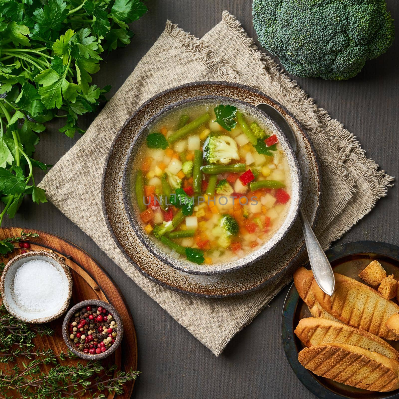 Vegetable soup, dietary vegetarian bright spring dish, linen napkin, top view, brown dark background.