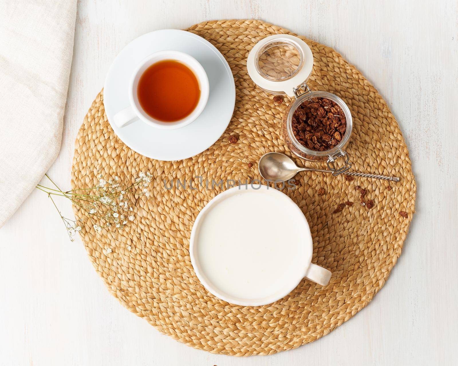 Yogurt with chocolate granola in cup, breakfast with tea on beige background, top view