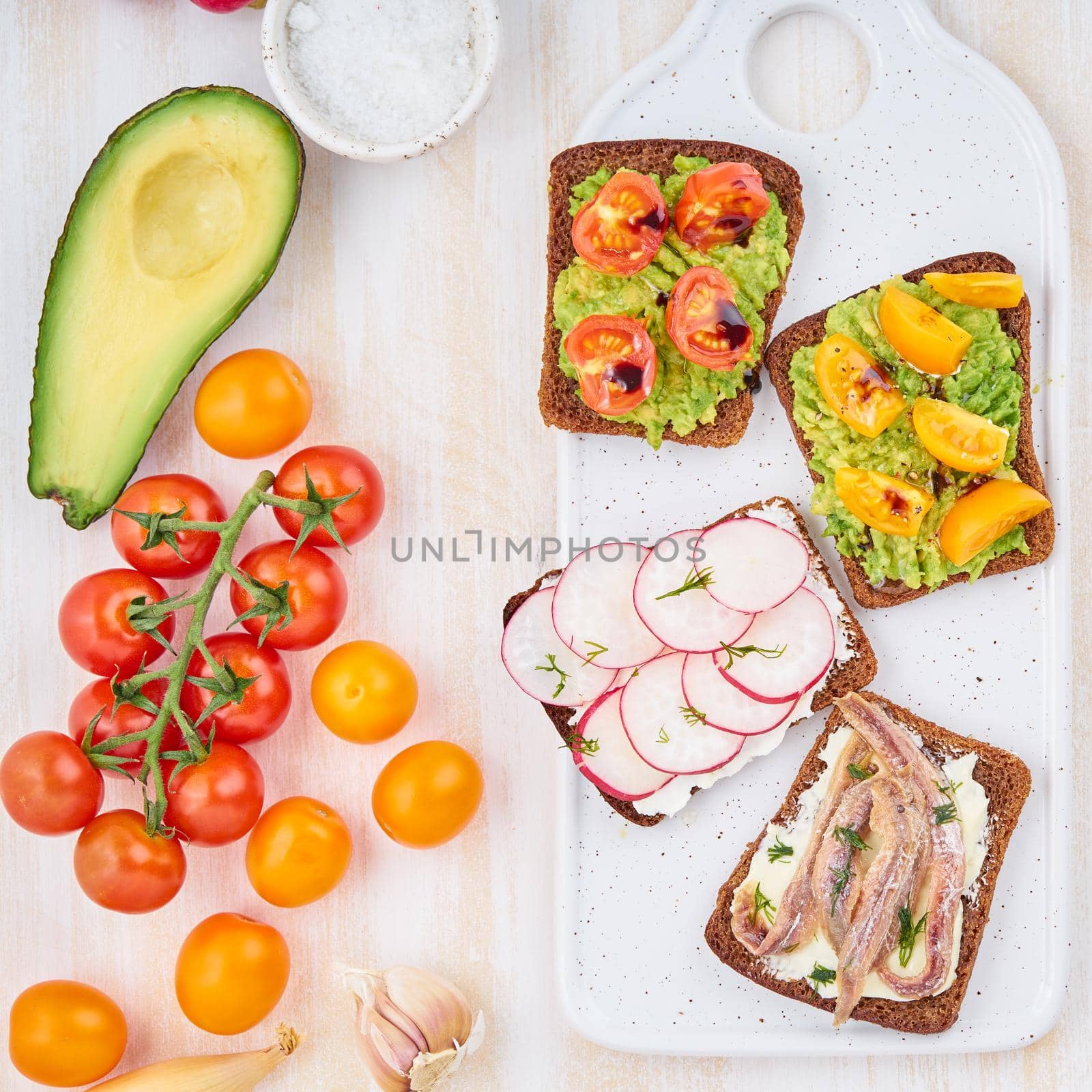 Set of smorrebrods with fish, anchovies, avocado, tomatoes, radish. Top view, white board, white background