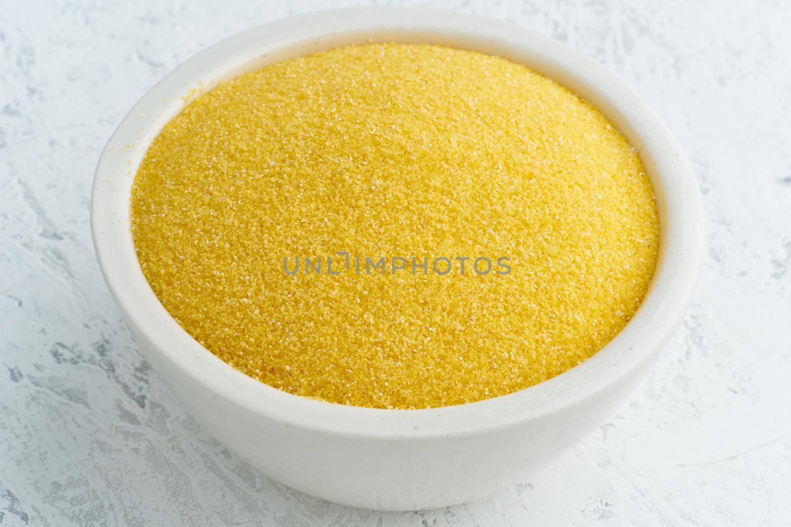 Corn, polenta in a white bowl on white background. Dried cereals in cup, vegan food, fodmap diet. Side view, close up.