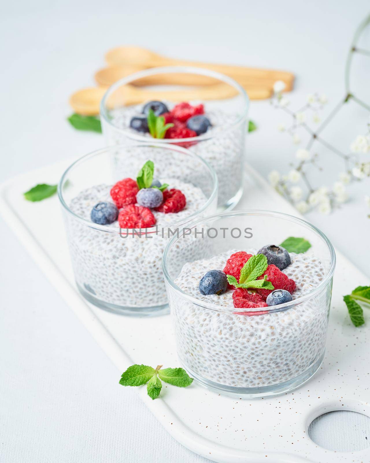 Chia pudding with fresh berries raspberries, blueberries. Three glass, light background, side view, flowers, vertical