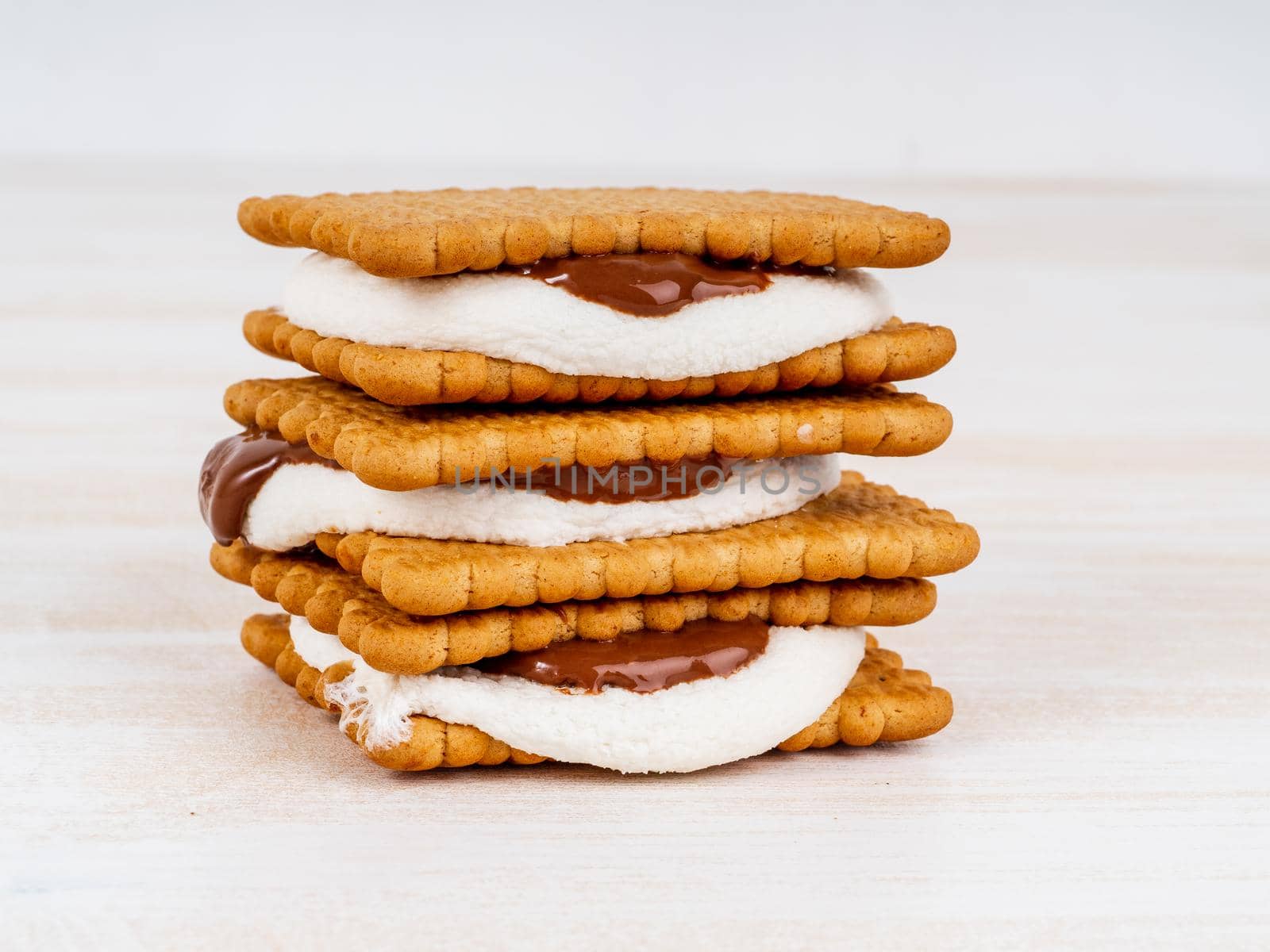 Smores, marshmallow sandwiches - traditional American sweet chocolate cookies on white wooden table, side view.