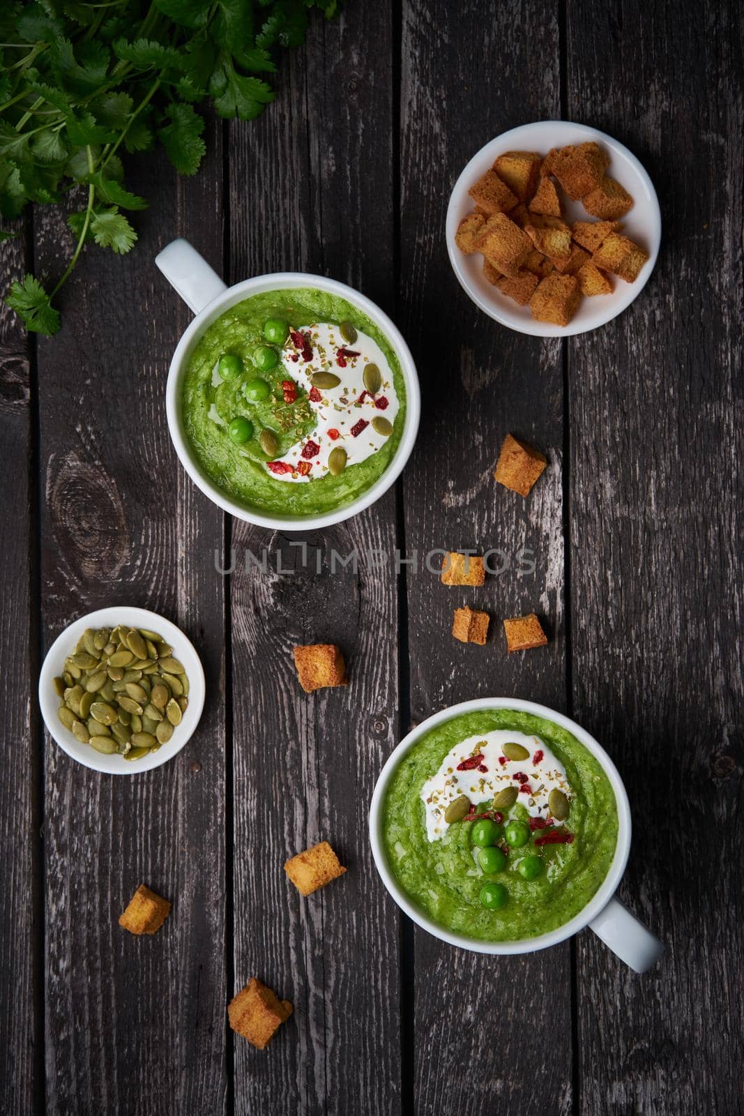 Broccoli cream soup on dark wooden background, vertical, copy space, top view. Vegetable green puree in two large white cup. Diet vegan soup of broccoli, zucchini, green peas by NataBene
