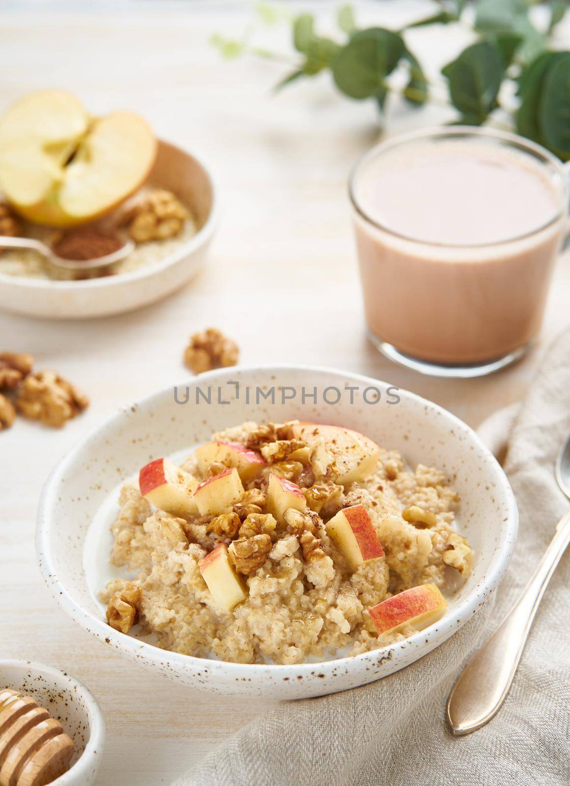 Oatmeal with apple, nuts, cinnamon, honey and cup of hot chocolate on white wooden light background. Vertical. Healthy diet breakfast
