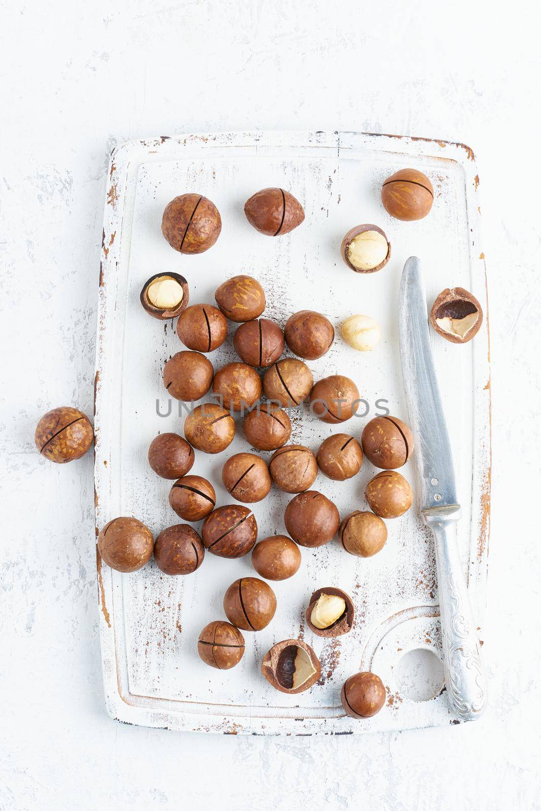 Plate with almonds in endocarp, whole and chopped open nuts in bulk on a cutting board with knife on a white background, top view.