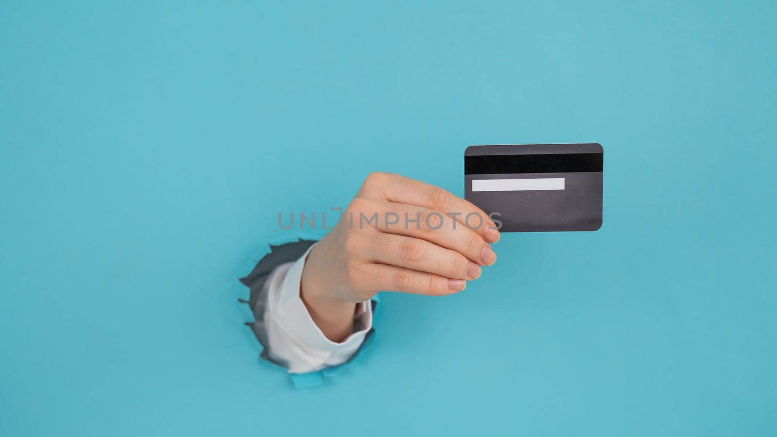A woman's hand sticking out of a hole in a paper blue background holds a credit card