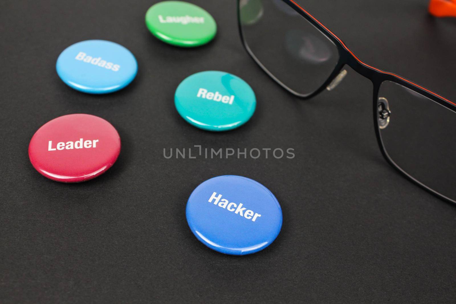 Colored plastic magnetic buttons on a black background next to glasses. Side view. Buttons with words leader, hacker, rebel, badass. by JuliaDorian