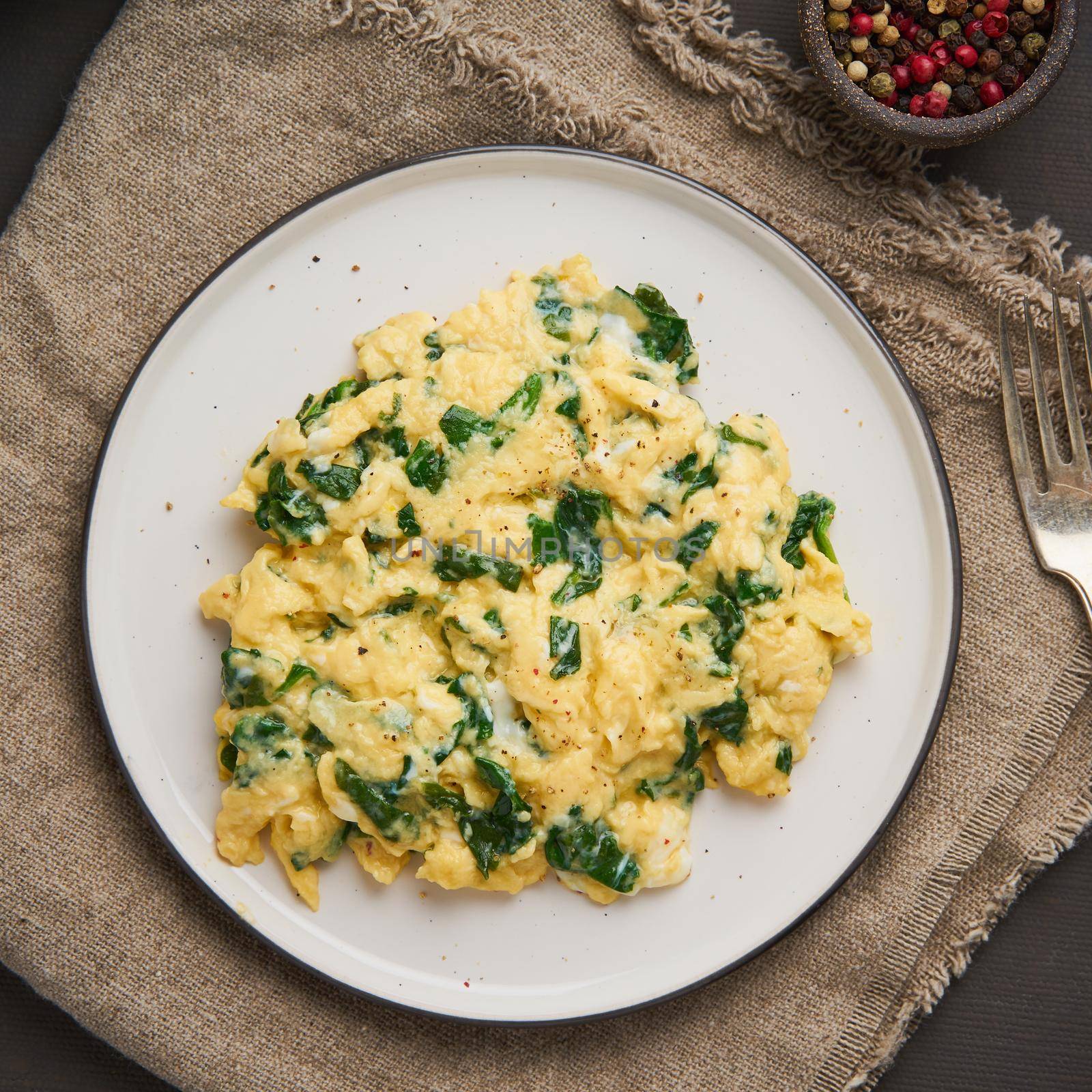 Pan-fried scrambled eggs and spinach, cup of tea on dark brown background. by NataBene