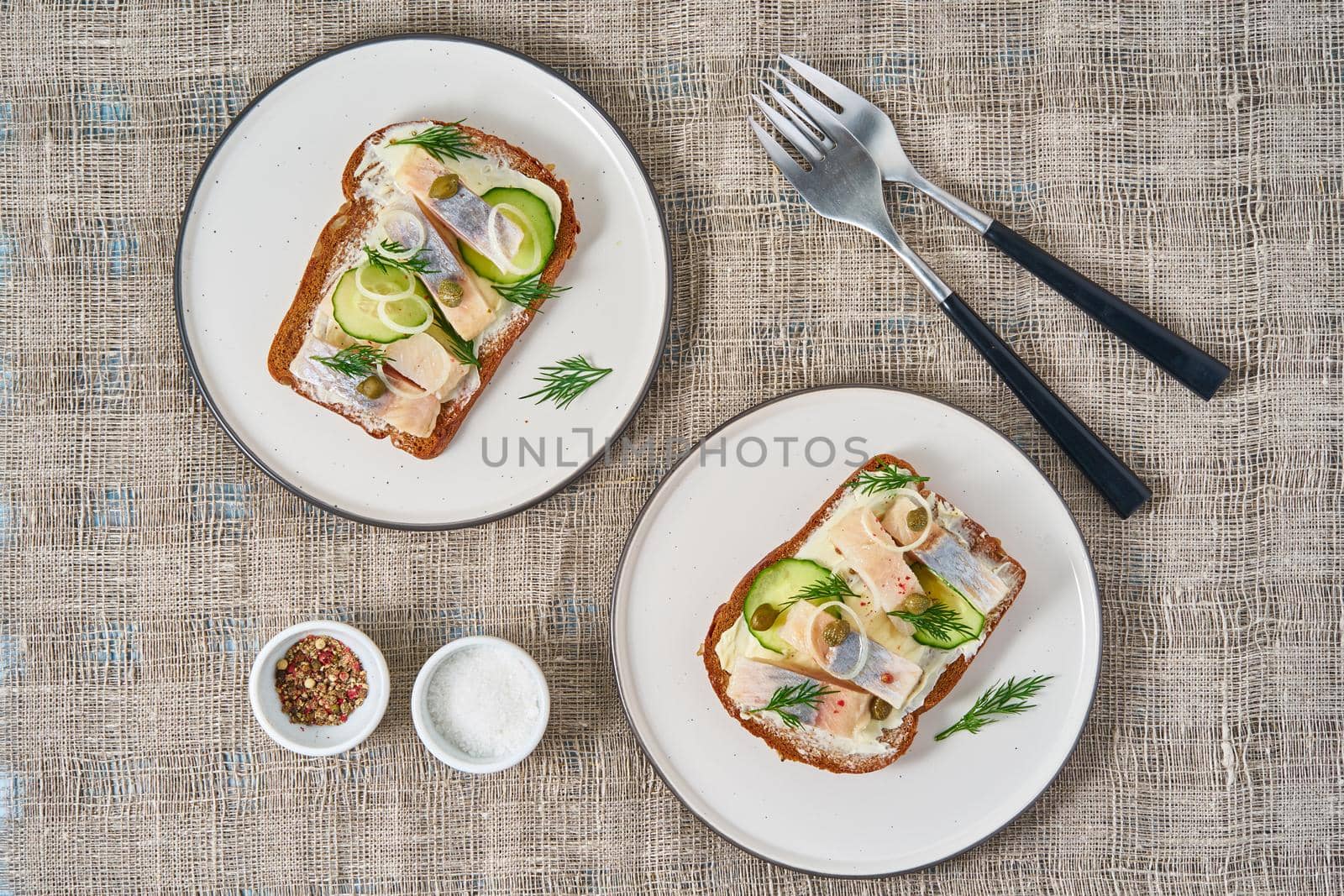 Herring smorrebrod - traditional Danish sandwiches. Two plate with black rye bread with herring on gray napkin, top view