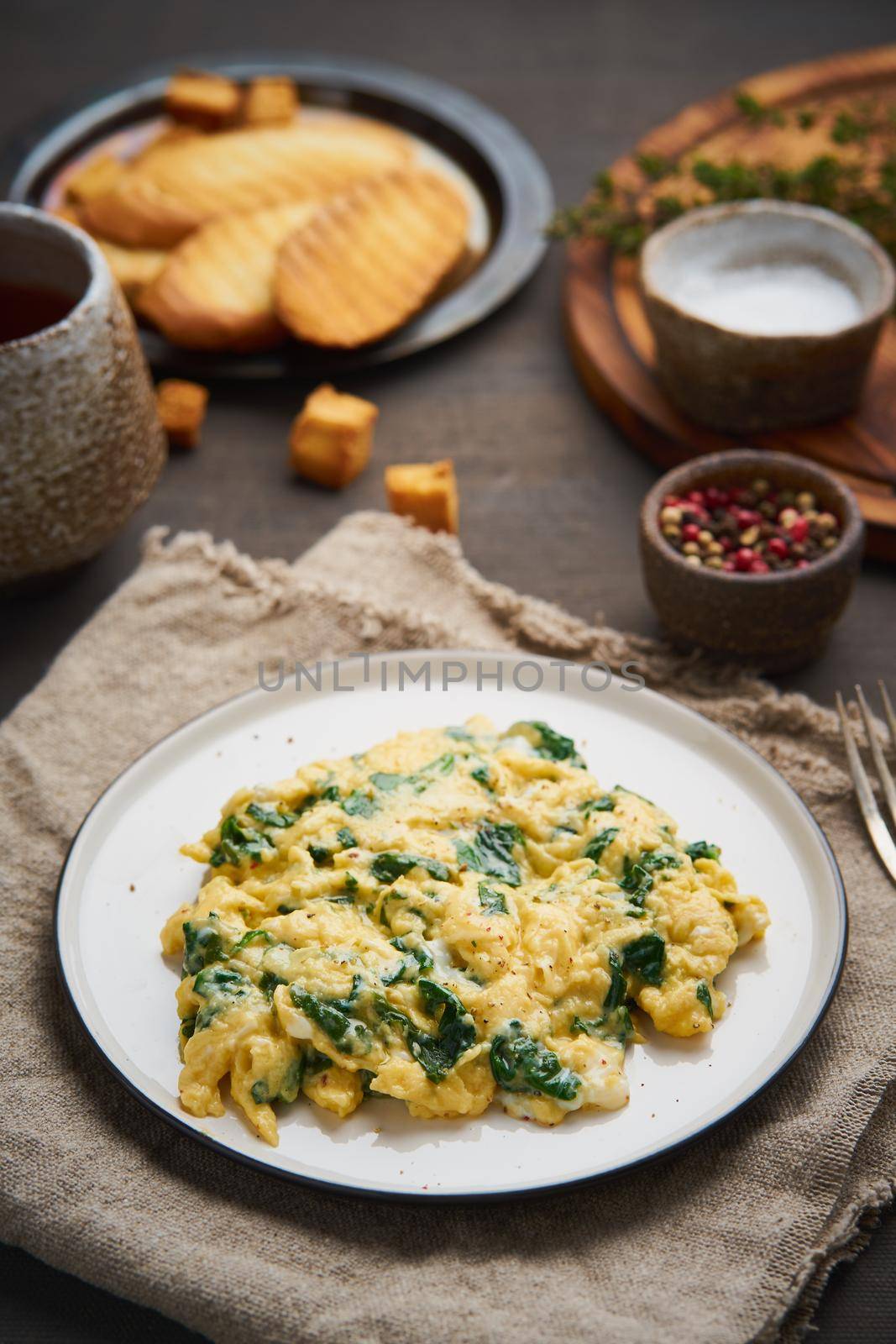 Scrambled eggs with spinach, cup of tea on dark brown background. Vertical by NataBene