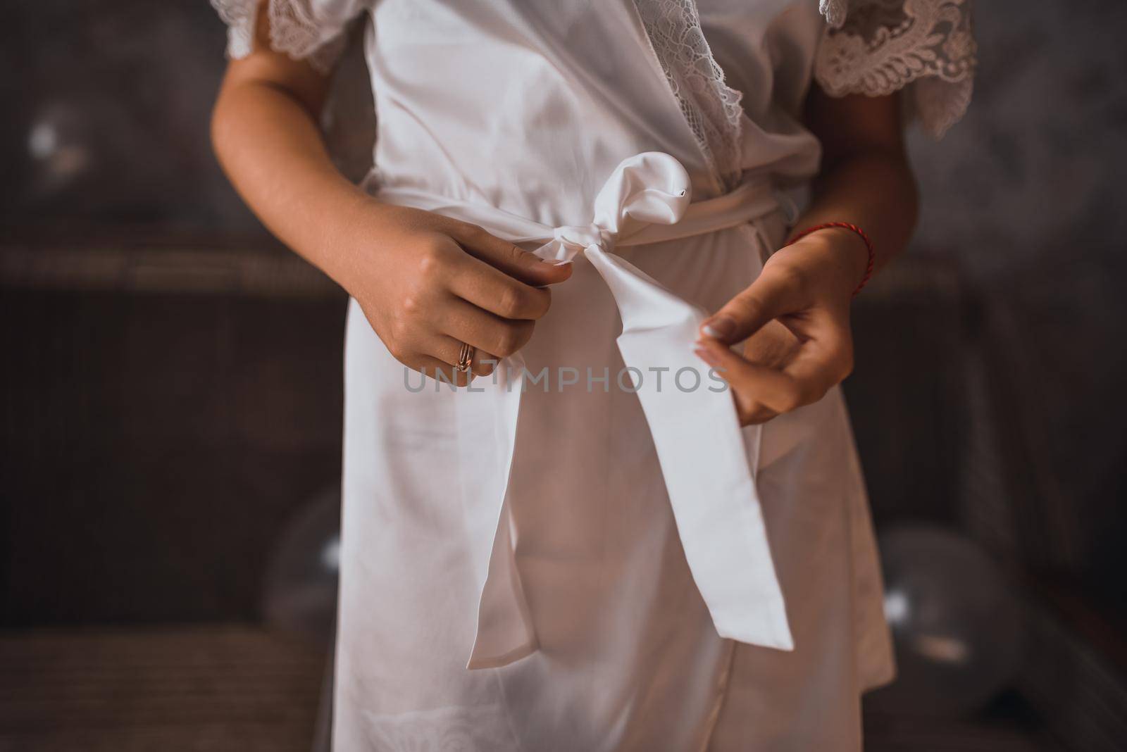 Young thin woman in pink silk robe unties the belt with her hands. bride in morning clothes