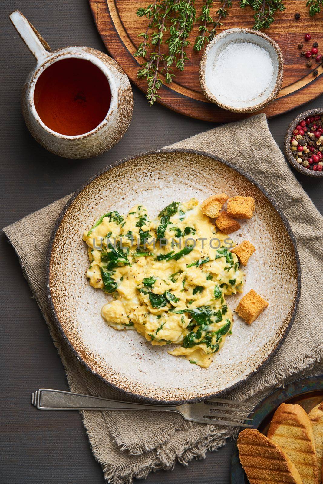 Scrambled eggs with spinach, cup of tea on dark brown background. Vertical. Breakfast with Pan-fried omelette, top view