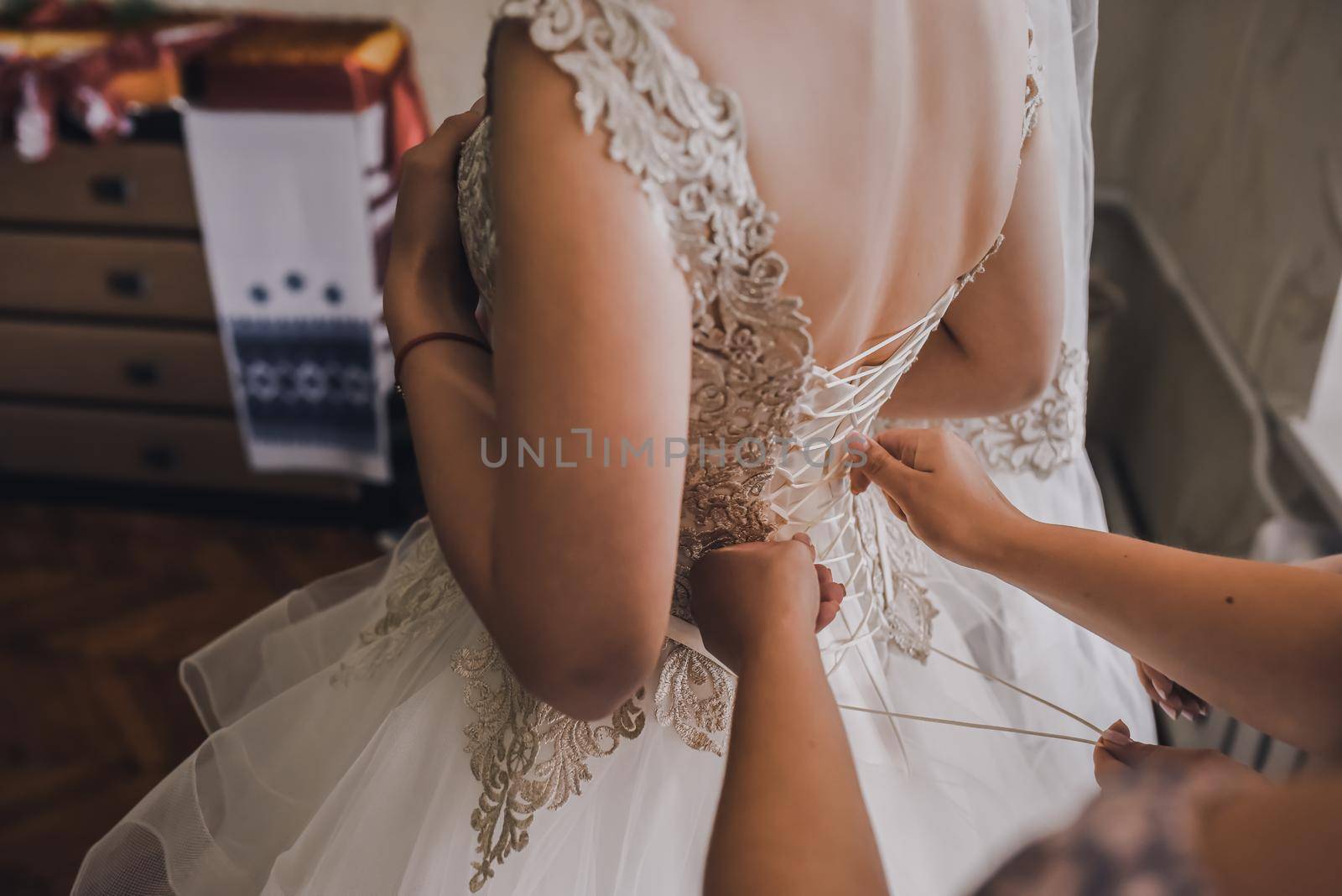 The back of the bride in a wedding dress. Mom's and woman's hands help fasten the clasps at the back.