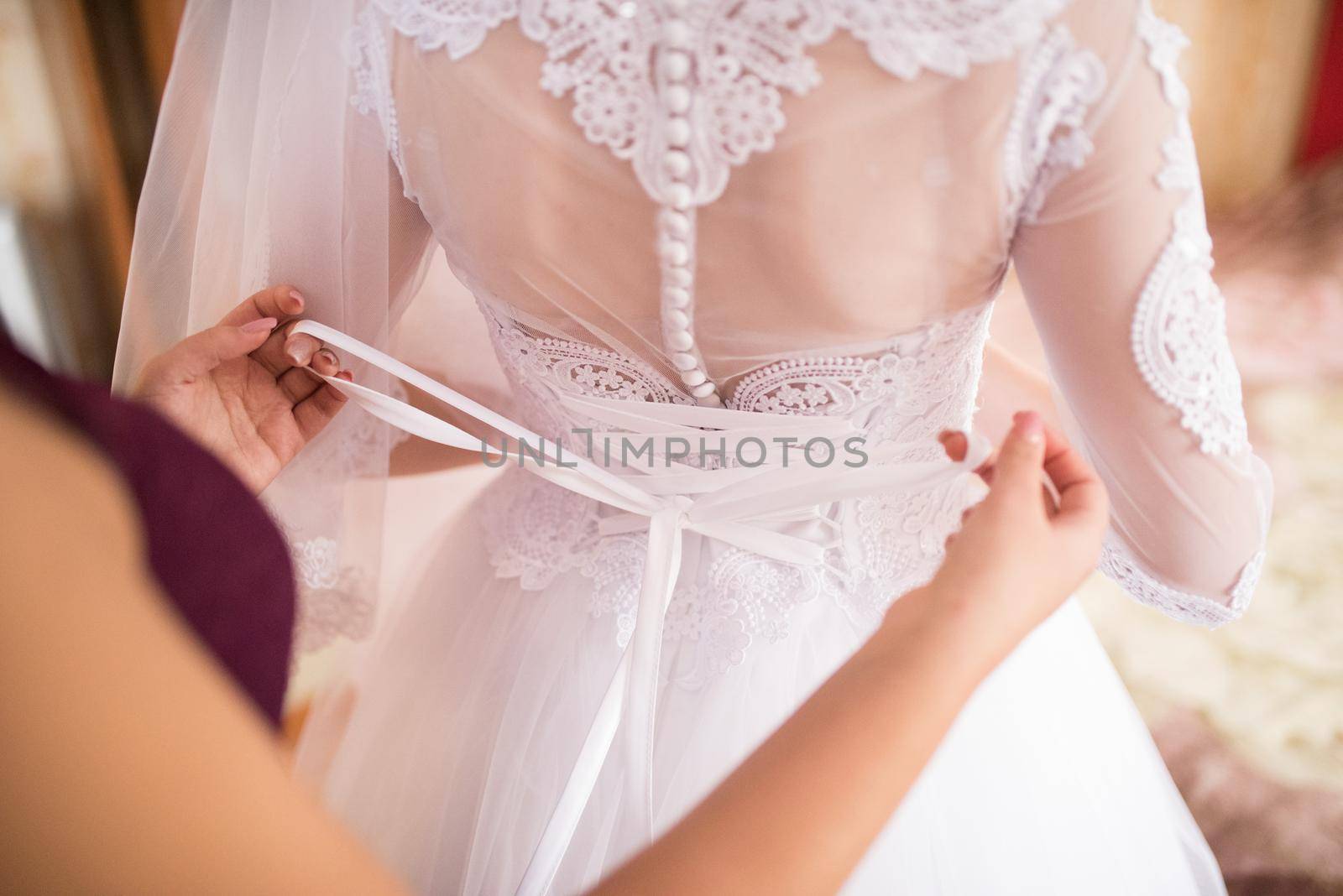 The back of the bride in a wedding dress. Mom's and woman's hands help fasten the clasps at the back.