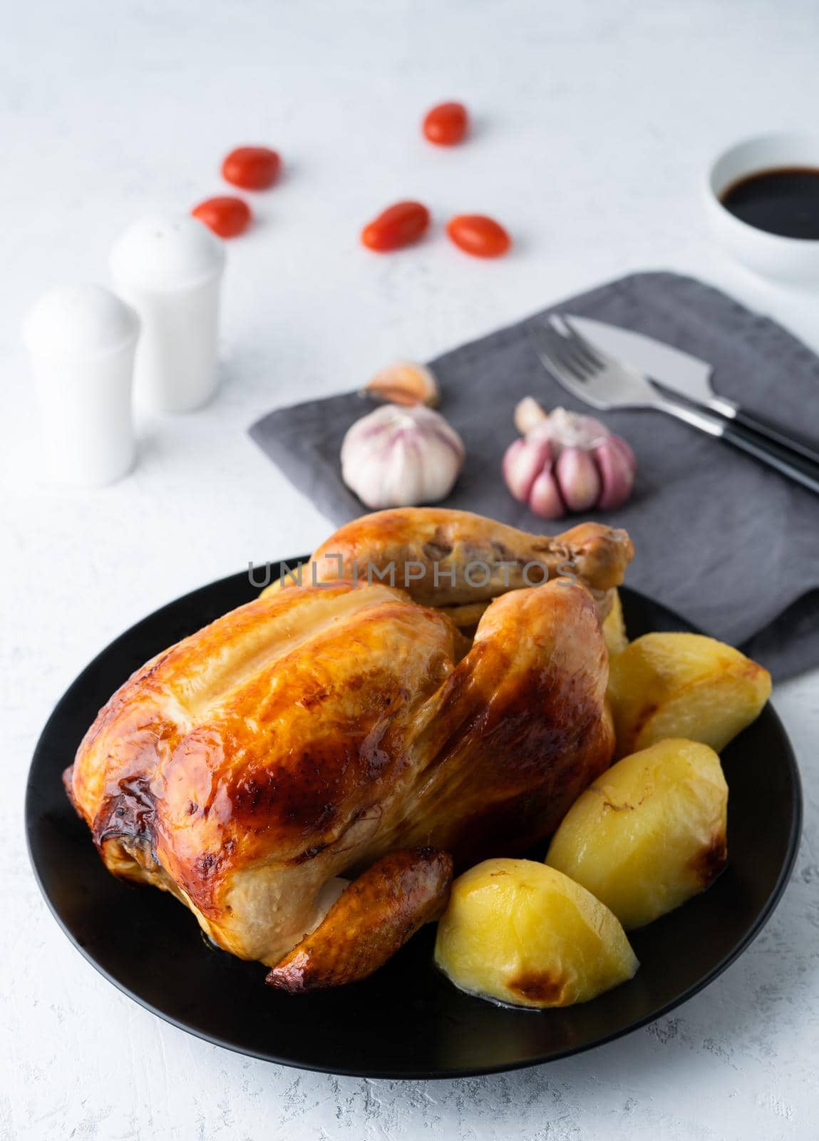 Grilled whole chicken in black plate on white table, baked meat with potatoes. Side view, vertical by NataBene