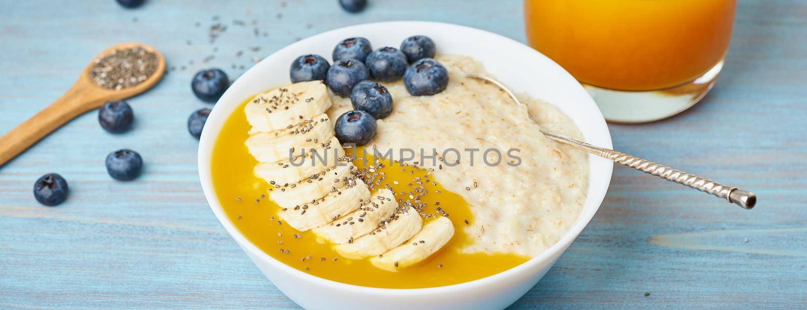 Banner with oatmeal, bananas, blueberries, chia seeds, mango jam on blue wooden background by NataBene