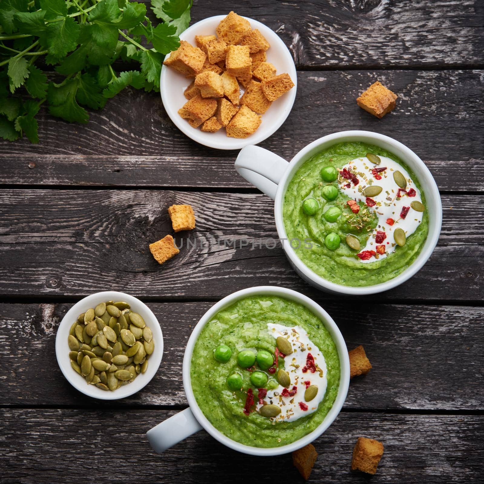 Broccoli cream soup, vegetable green puree in two large white cup. Diet vegan soup of broccoli, zucchini, green peas on dark wooden background, top view.