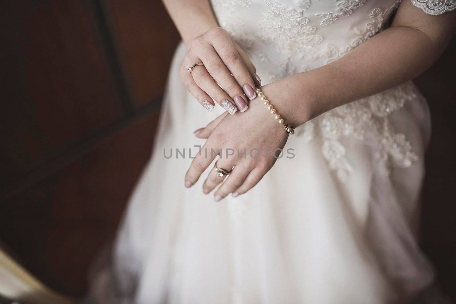 The female hands of the fair-skinned bride lie on the white wedding dress. A ring on the hand of a young girl.