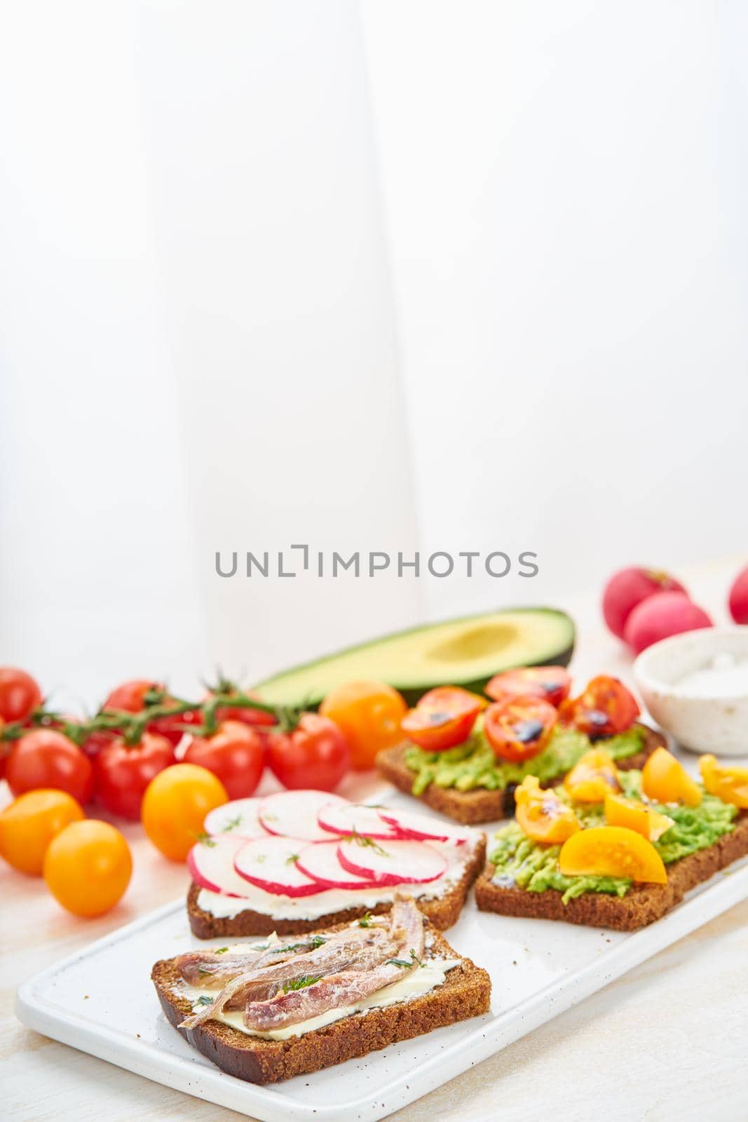 Set of smorrebrods with fish, anchovies, avocado, tomatoes, radish. Side view, copy space, white background.