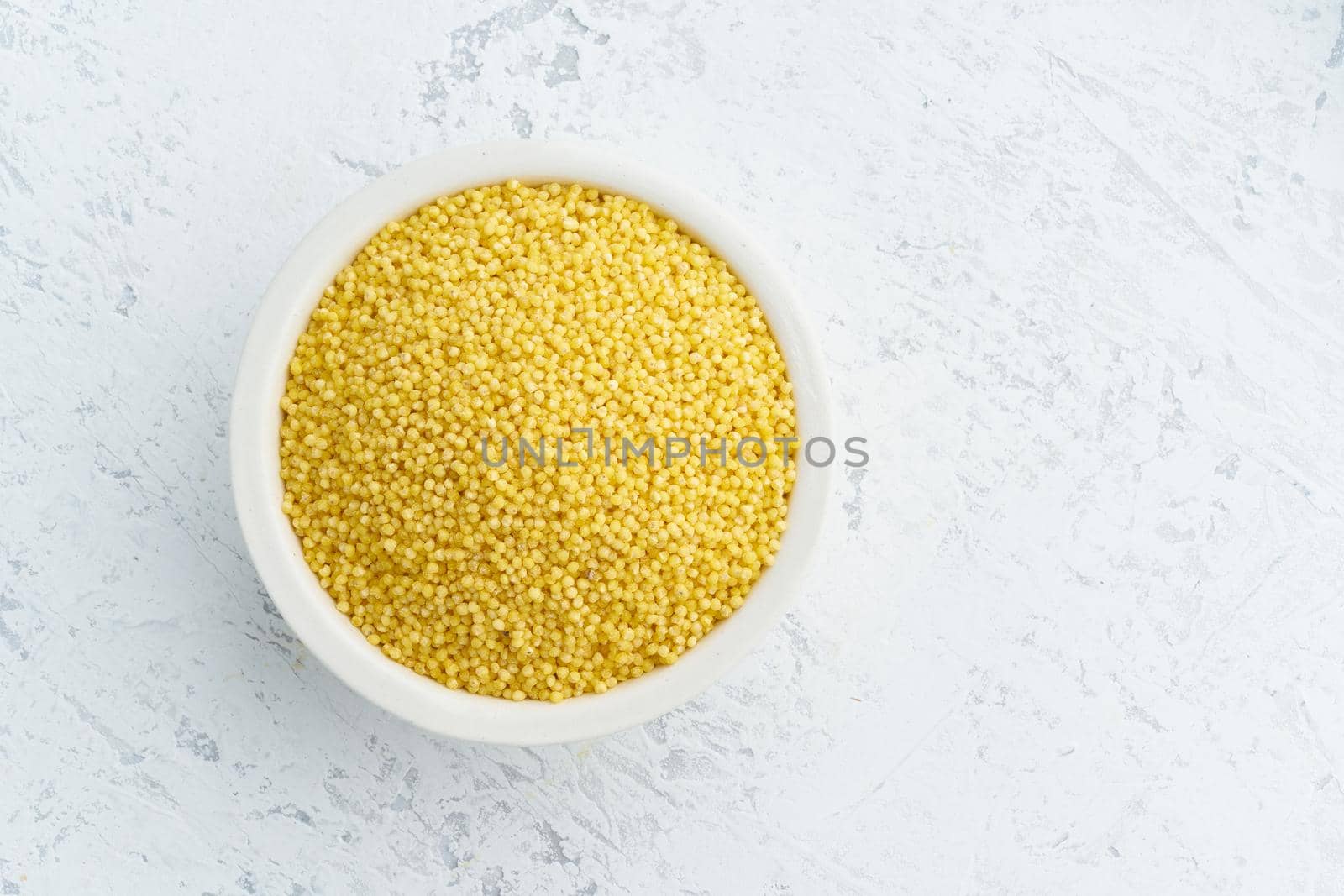 Millet, bulrush in a white bowl on white background. Lectine free, dried cereals in cup, vegan food, fodmap diet. Top view, close up.